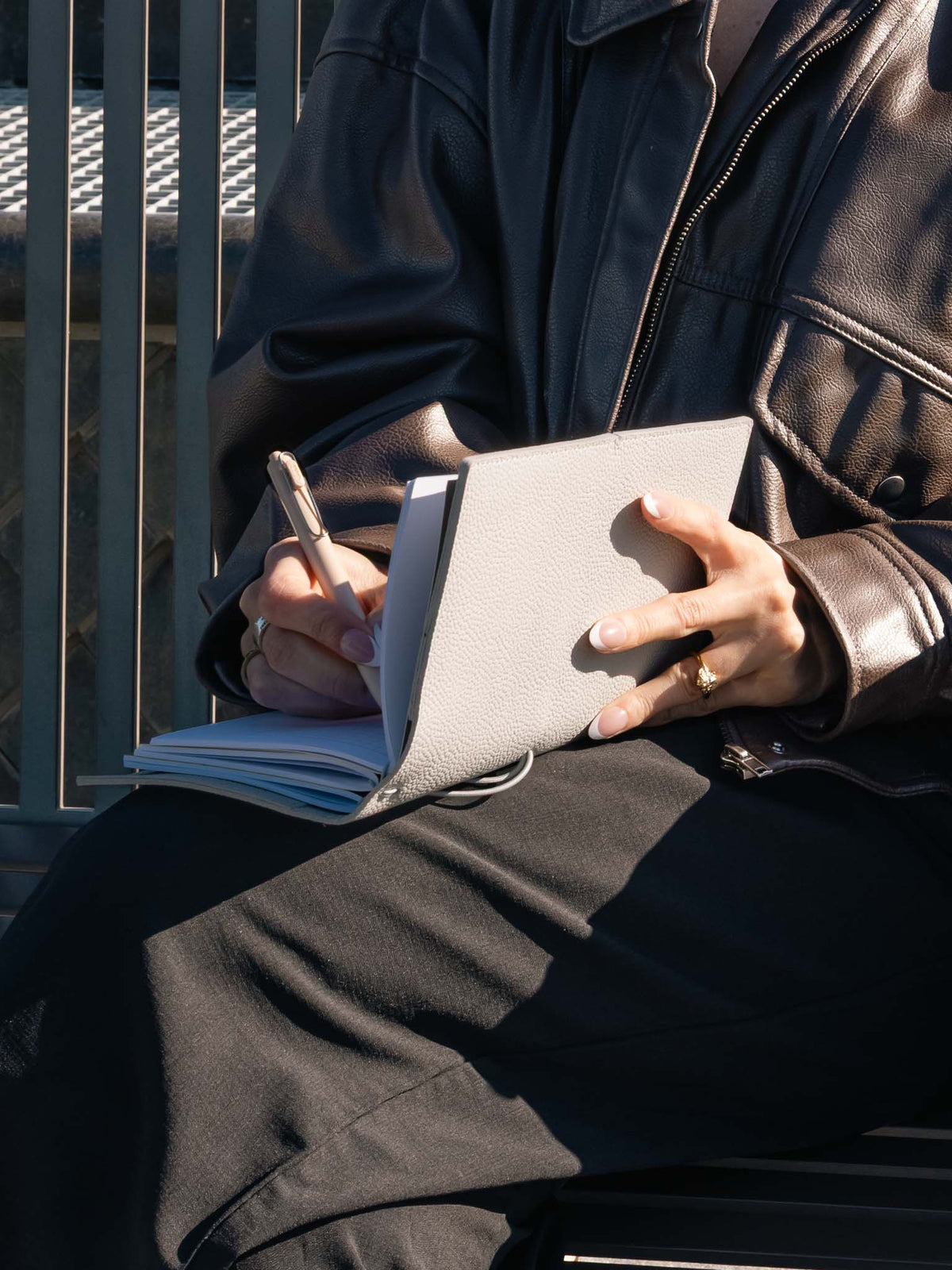A woman writing in a notebook that uses a light grey genuine leather travel notebook cover.