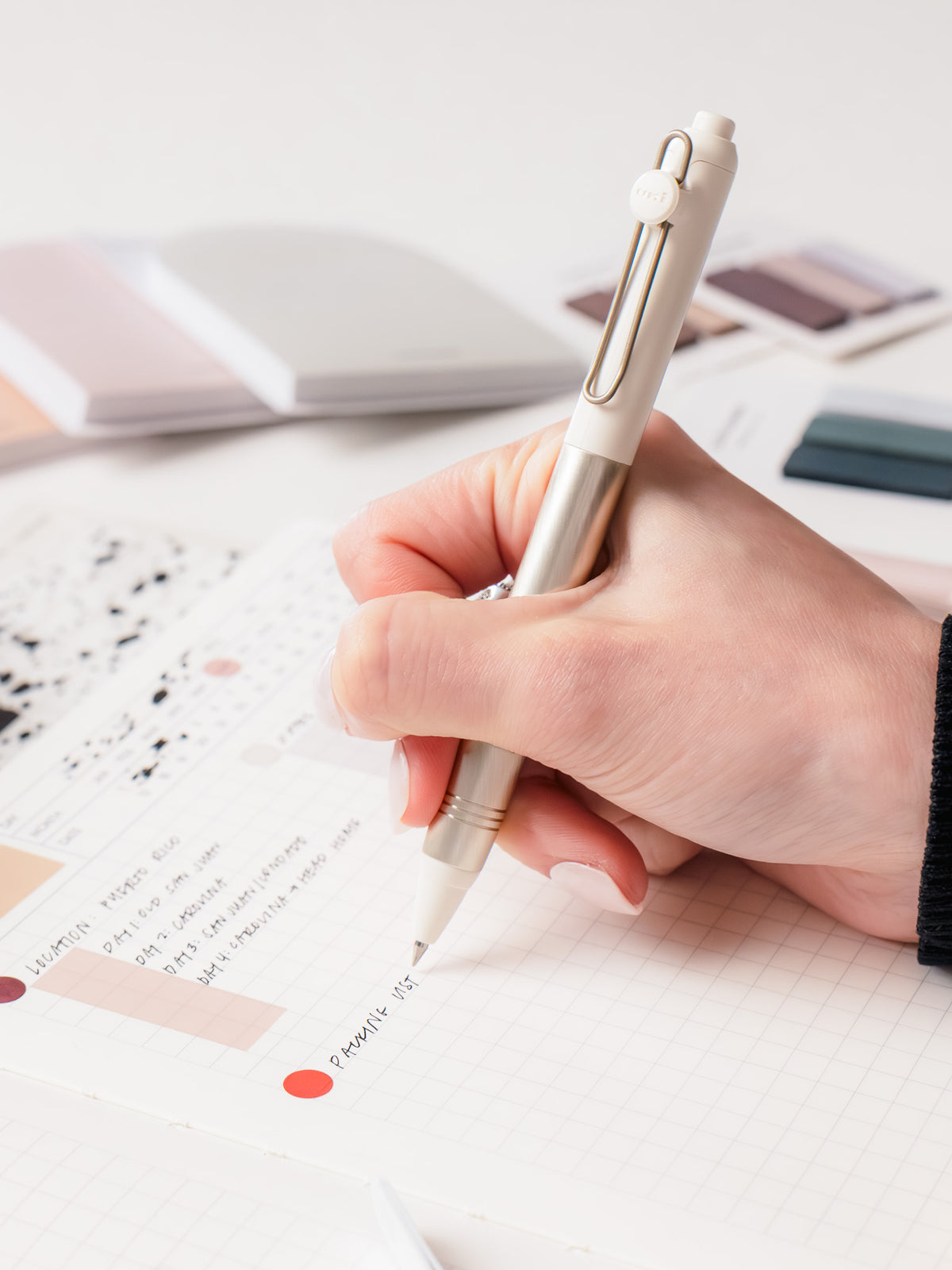 Woman writing in a notebook using the Uni-Ball Zento Flow Ballpoint Pen | Retreat Edition in the color Birch White with a 0.38 mm nib.