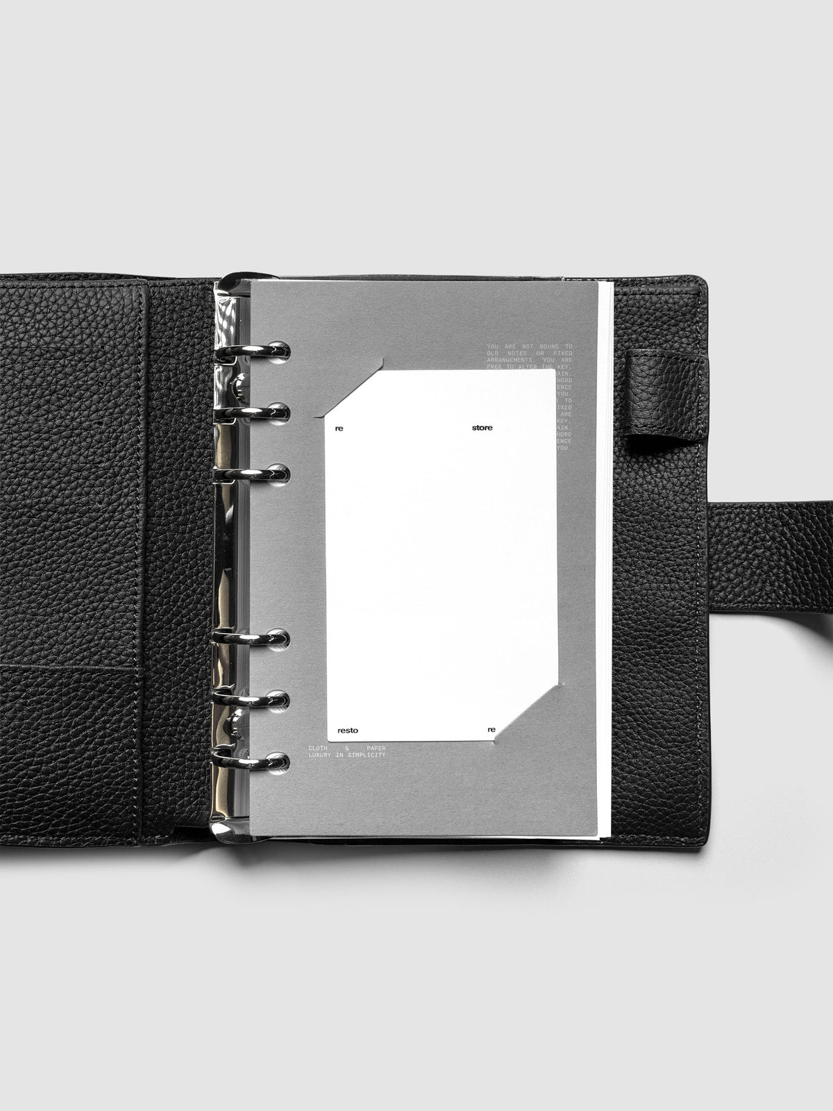 Grey cardstock planner dashboard with white plastic card inserted in slits with white printed text shown in size Personal shown in a ring bound planner.