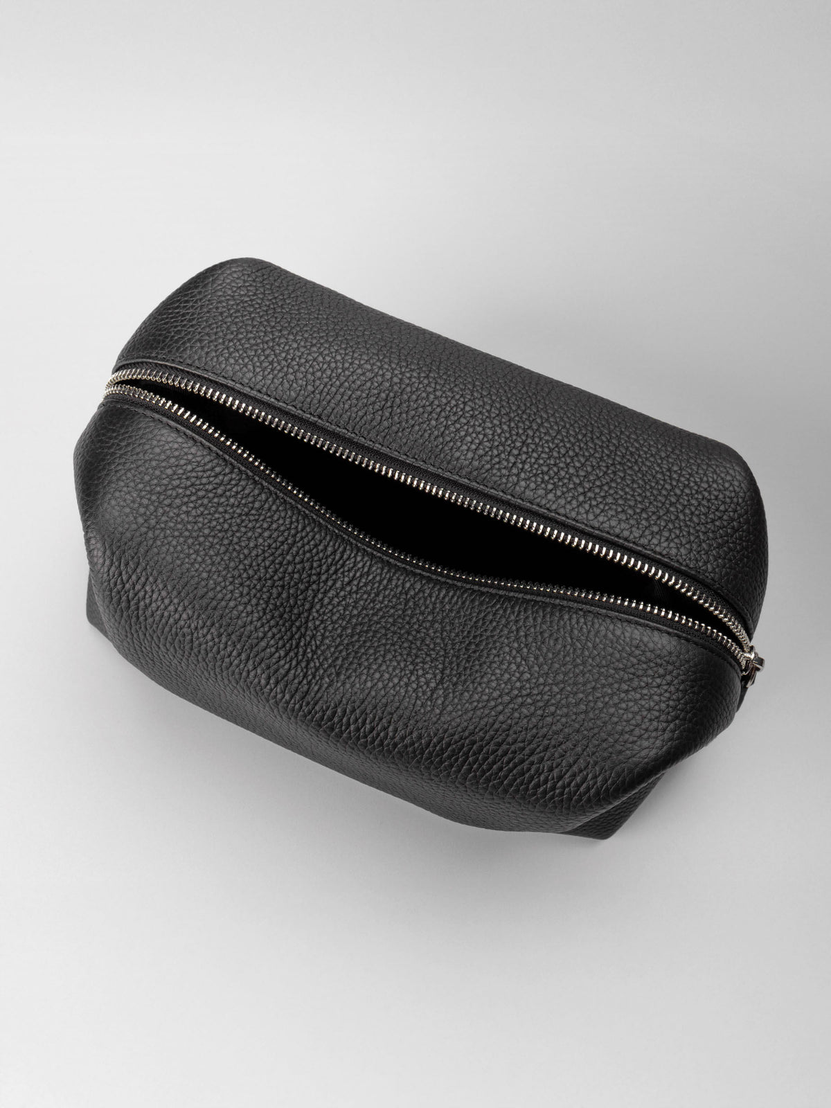 Folded Form Pouch in black pebbled leather, top-down view, unsnapped and open showing silver zipper partially unzipped