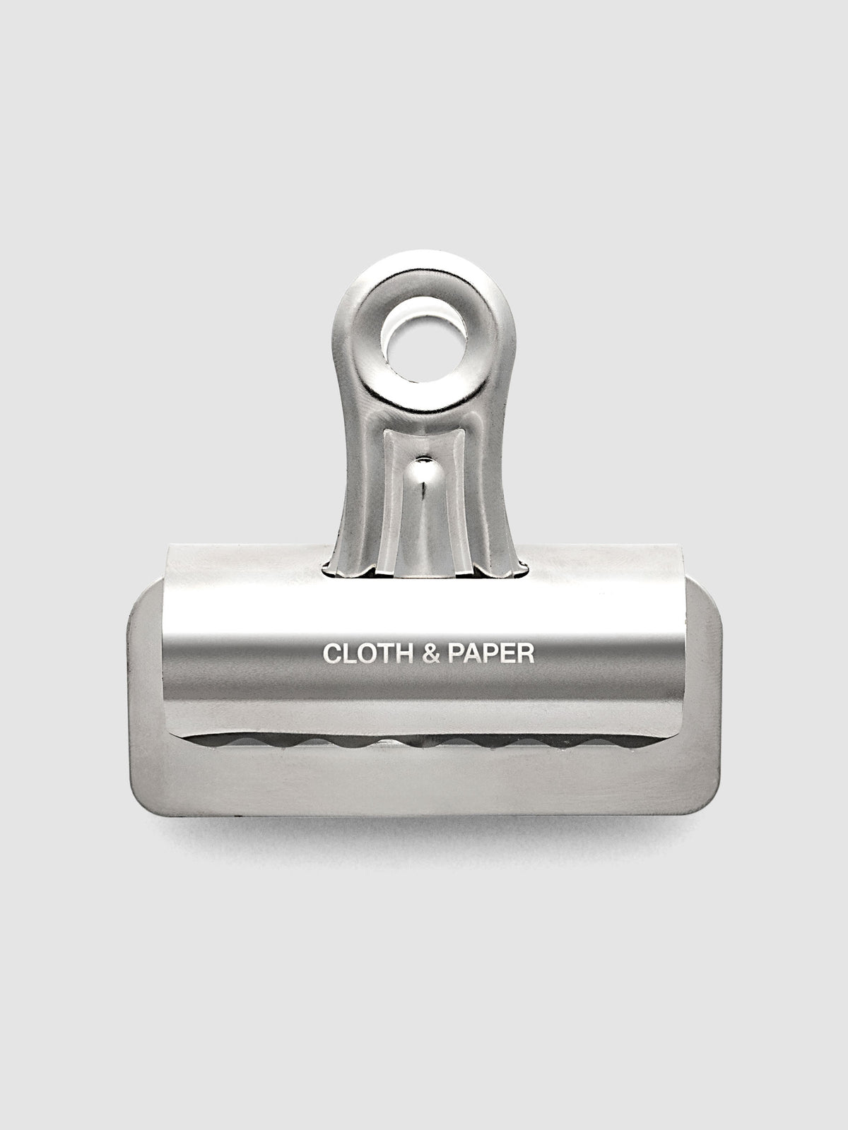 Silver metal notebook clip with Cloth & Paper logo etched onto the surface.