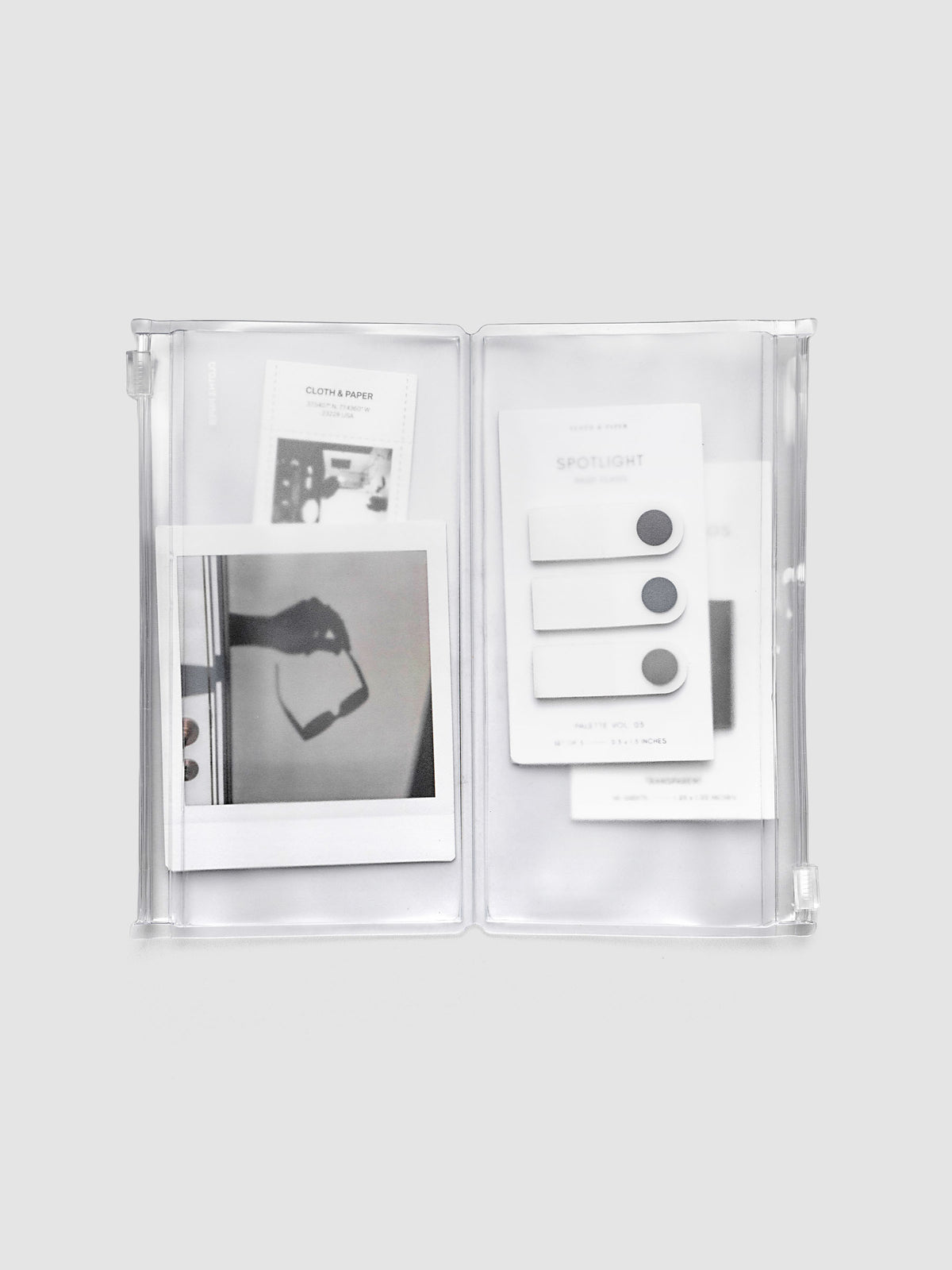 Pocket Plus travel notebook storage holder in clear frosted plastic, open, showing two zippered pouches with stickers and cards inside