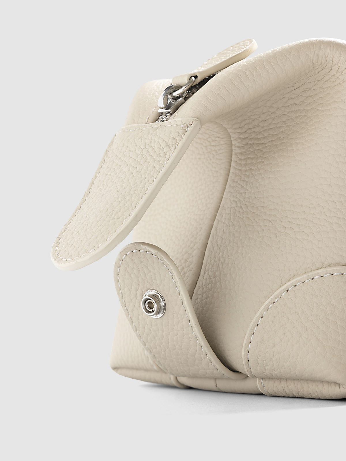Folded Form Pouch in warm beige pebbled leather, close-up of silver snap hardware on side panel with leather zipper pull and silver zipper visible above