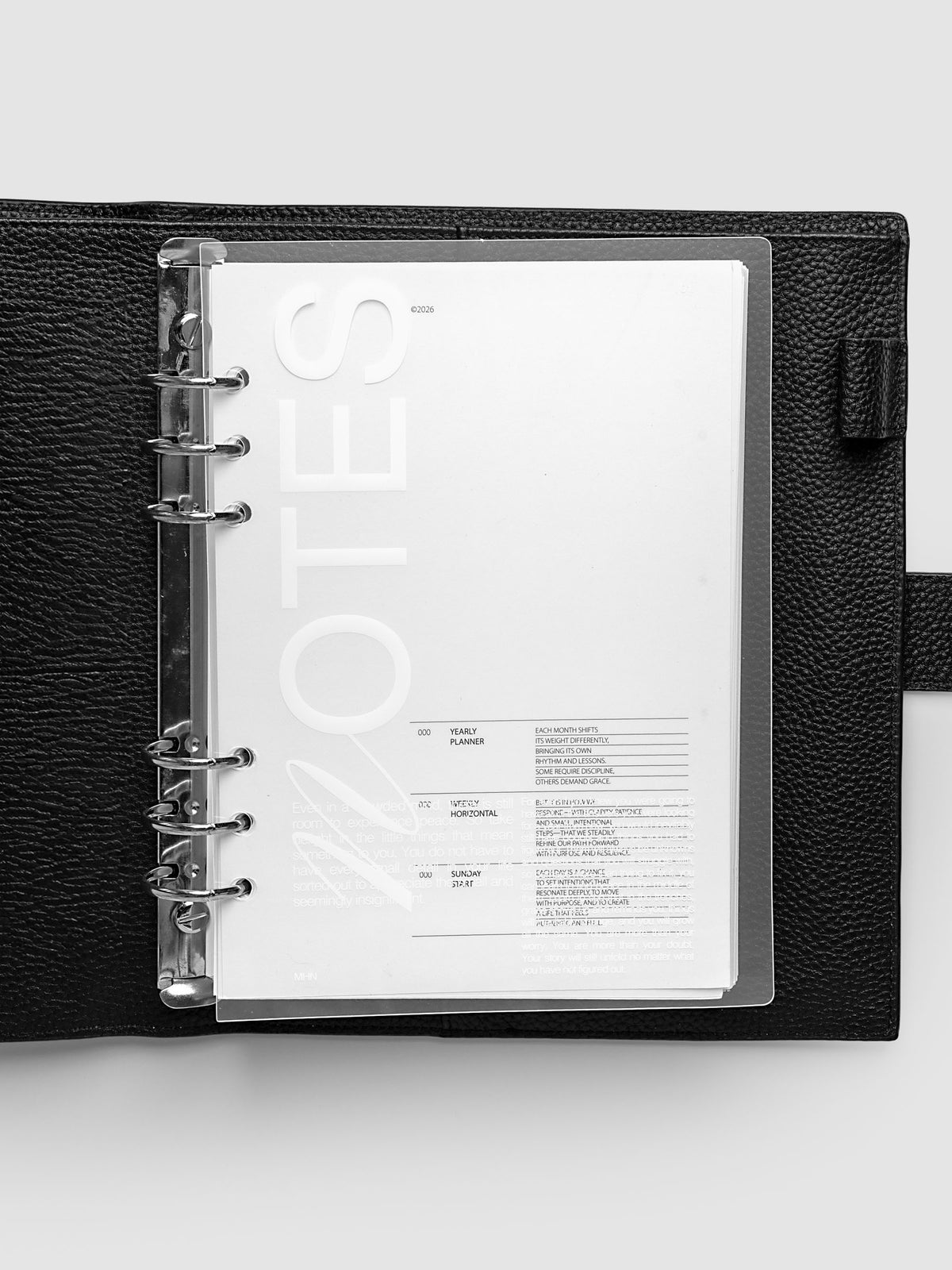 Clear plastic planner cover with white printed text shown pre-punched for A5 6-ring planners in a black agenda.