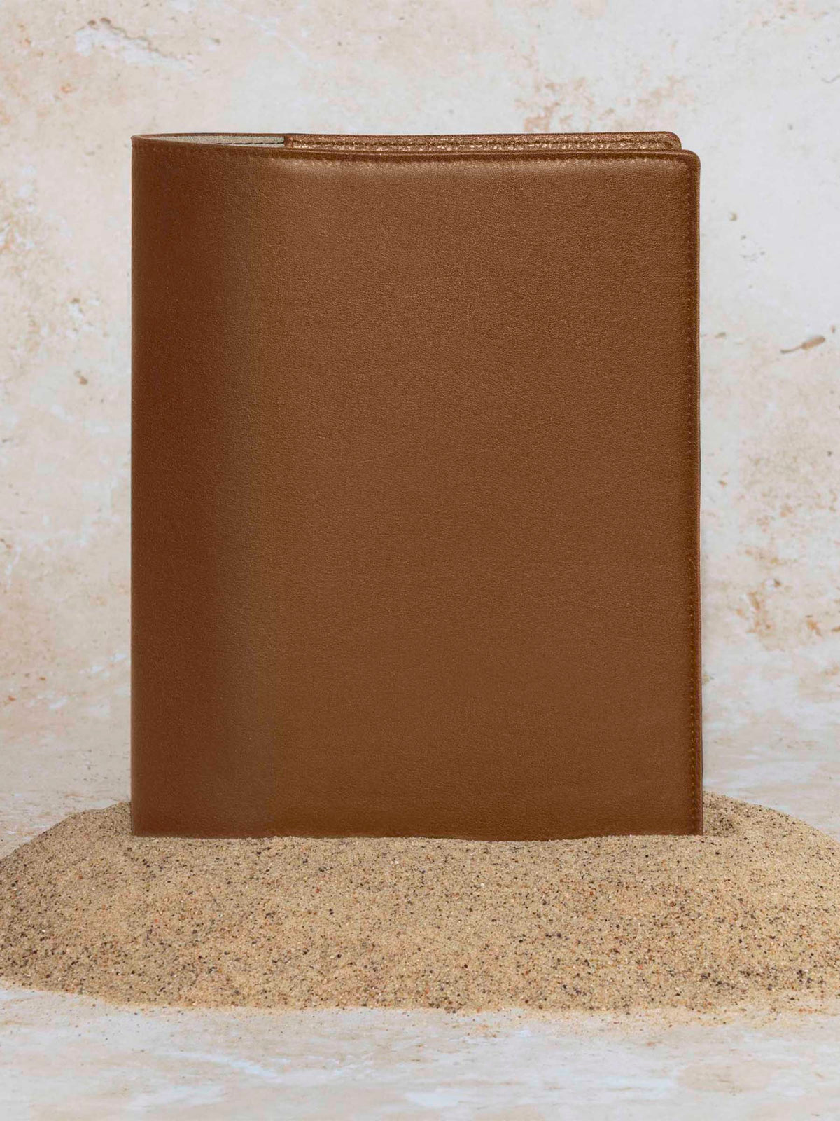 Folio displayed on a textured tan background, placed in a pile of sand. Color pictured is clay brown.