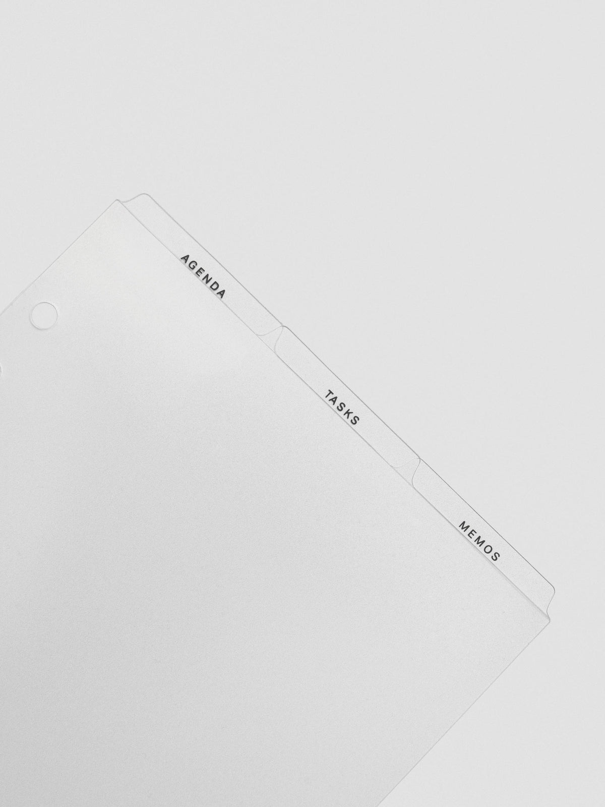 Angled close-up of the ultra-thin clear planner dividers showing top tabs labeled Agenda, Tasks, and Memos.