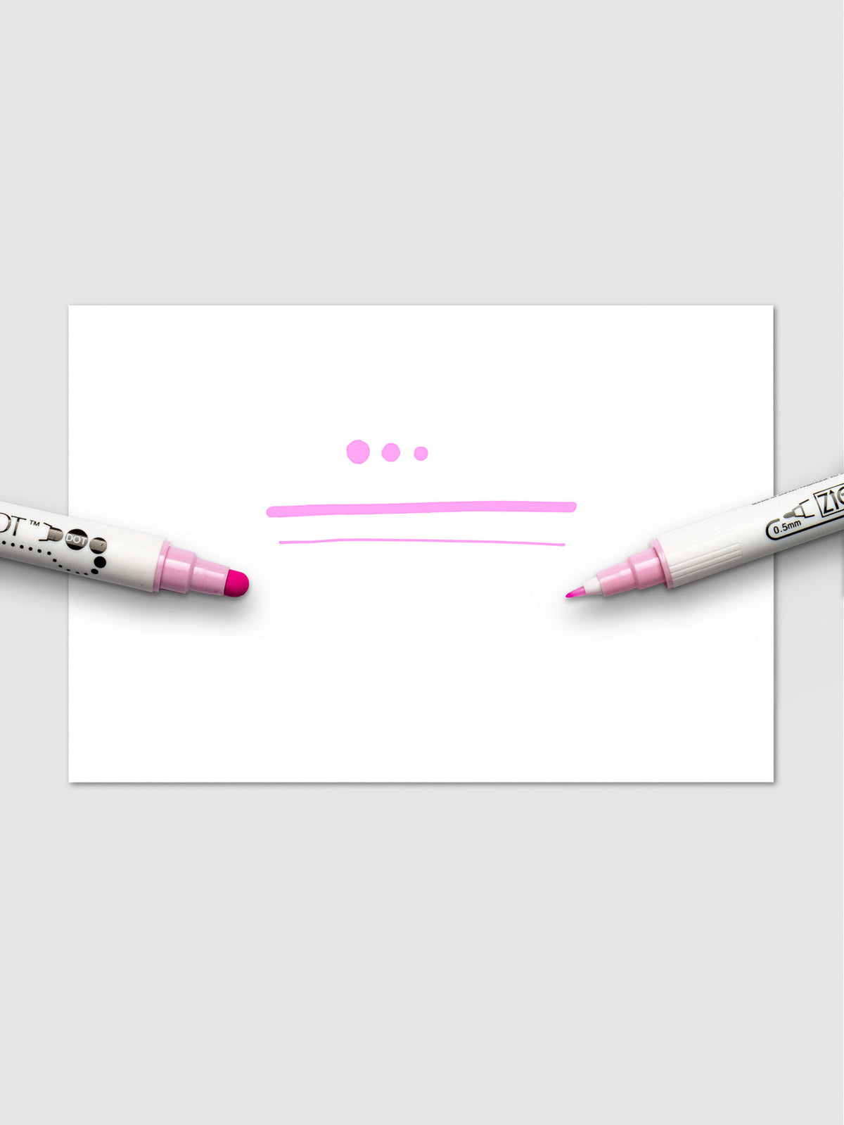 Sample writing in pink ink demonstrating the marker's dot and fine tip capabilities on a white sheet.