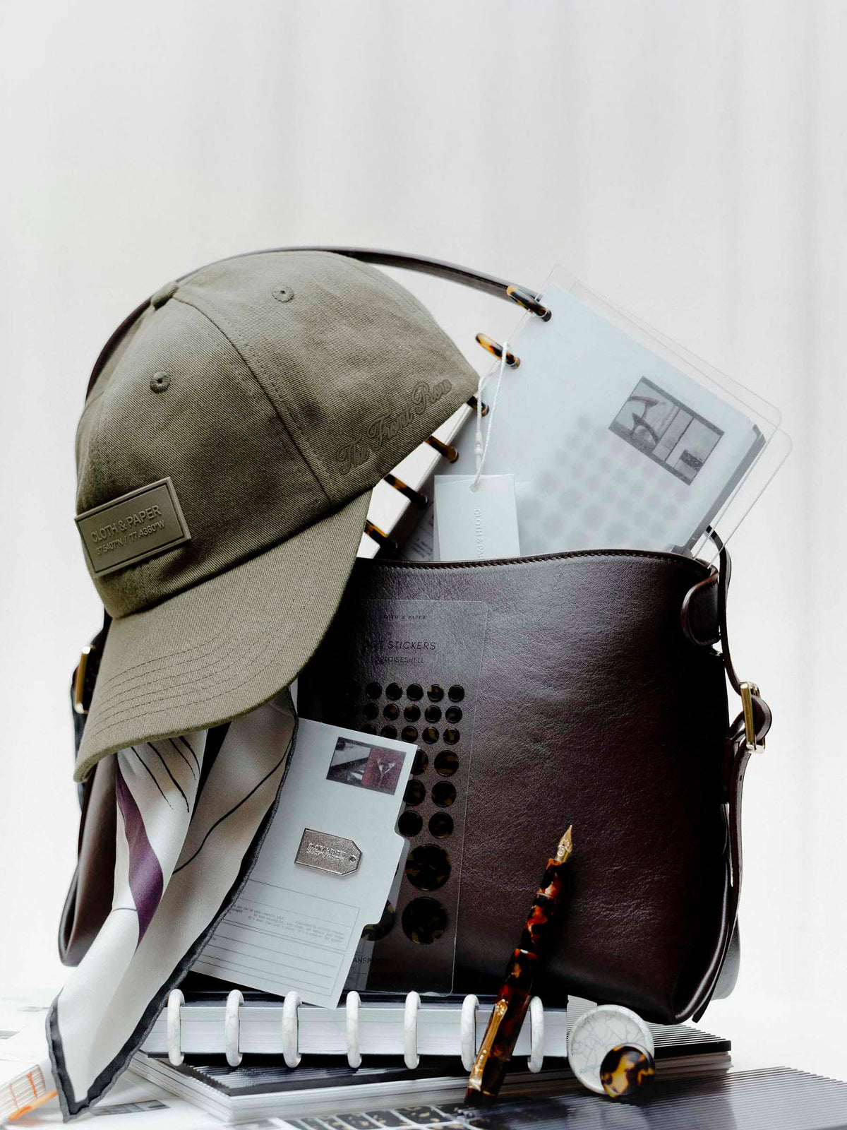 Several Planner Essentials and accessories from the Front Row Collections staged inside a Valencia Bag. Heavily featured are the Label Hat, Planner Brooch | Tag, and Kaweco Art Sport Fountain Pen in Hickory Brown.