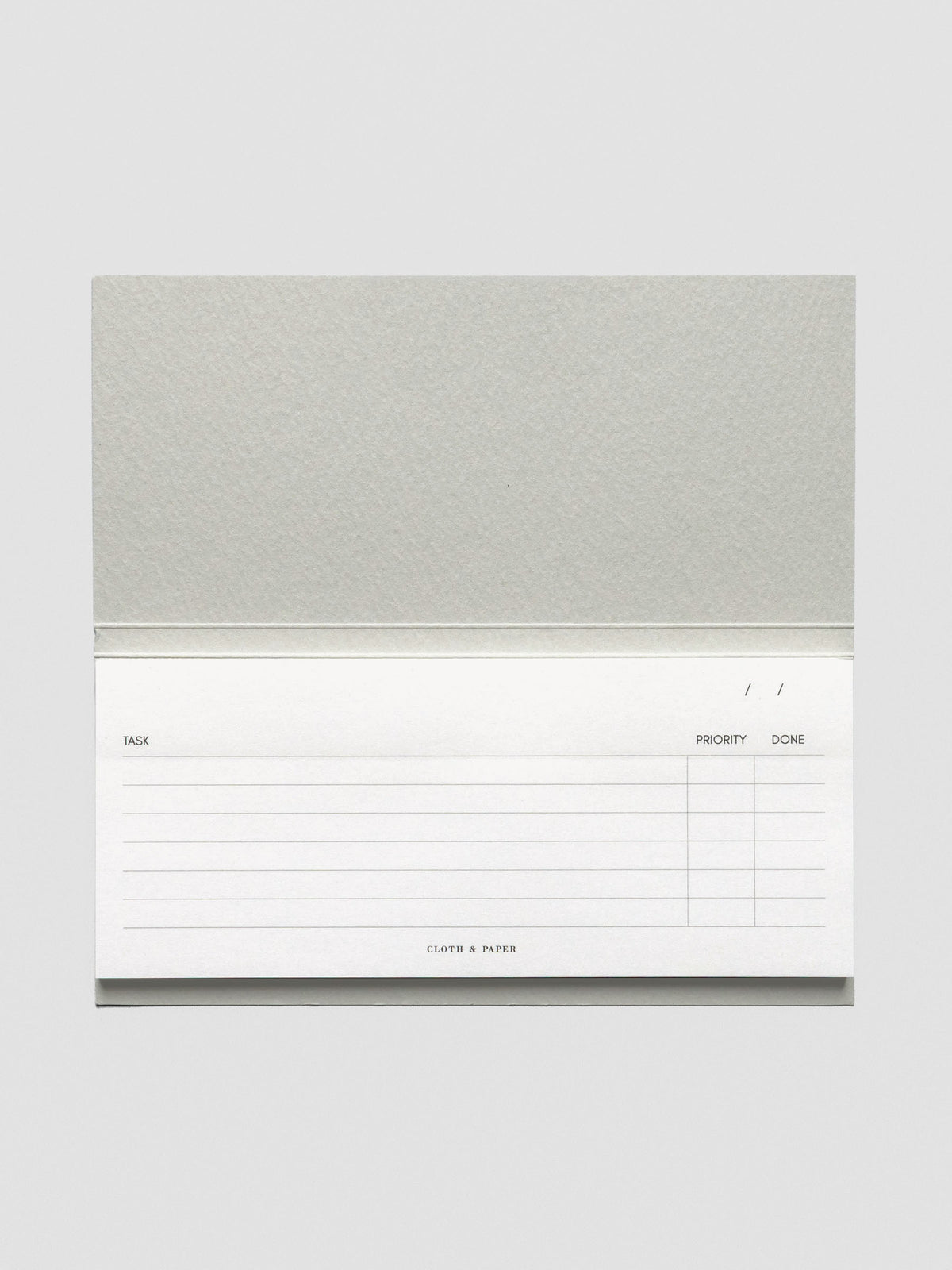 Horizontal view of the notepad fully open, highlighting its landscape layout and structured task, priority, and completion columns with subtle branding at the bottom.