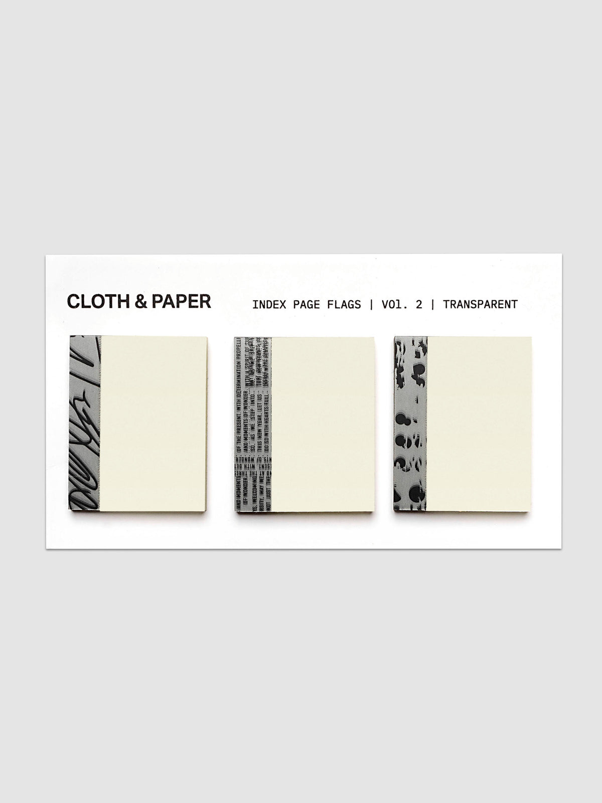 Three cream-colored index page flags with black printed text and patterned borders, displayed on a white card labeled 'CLOTH & PAPER INDEX PAGE FLAGS | VOL. 2 | TRANSPARENT' against a light gray background.