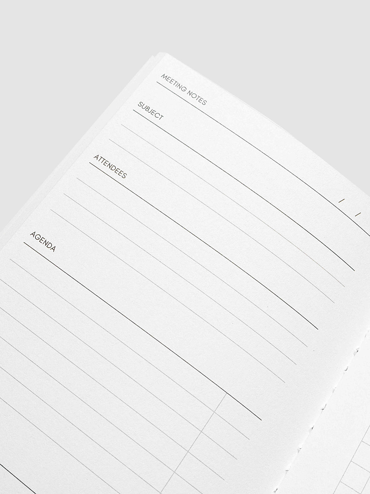 A close-up of an open planner or notebook page with lined meeting notes sections labeled Meeting Notes, Subject, Attendees, and Agenda on a light gray background.