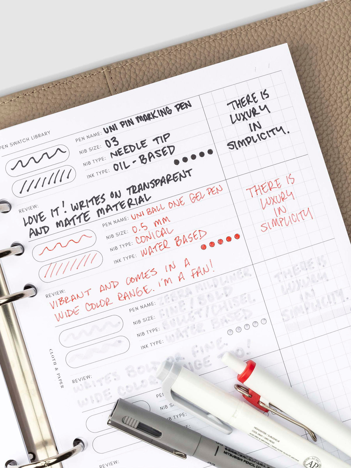 Inserts in use inside of a 6-ring binder. There are writing swatches for three pens filled out. The three pens tested are resting on the bottom of the insert.