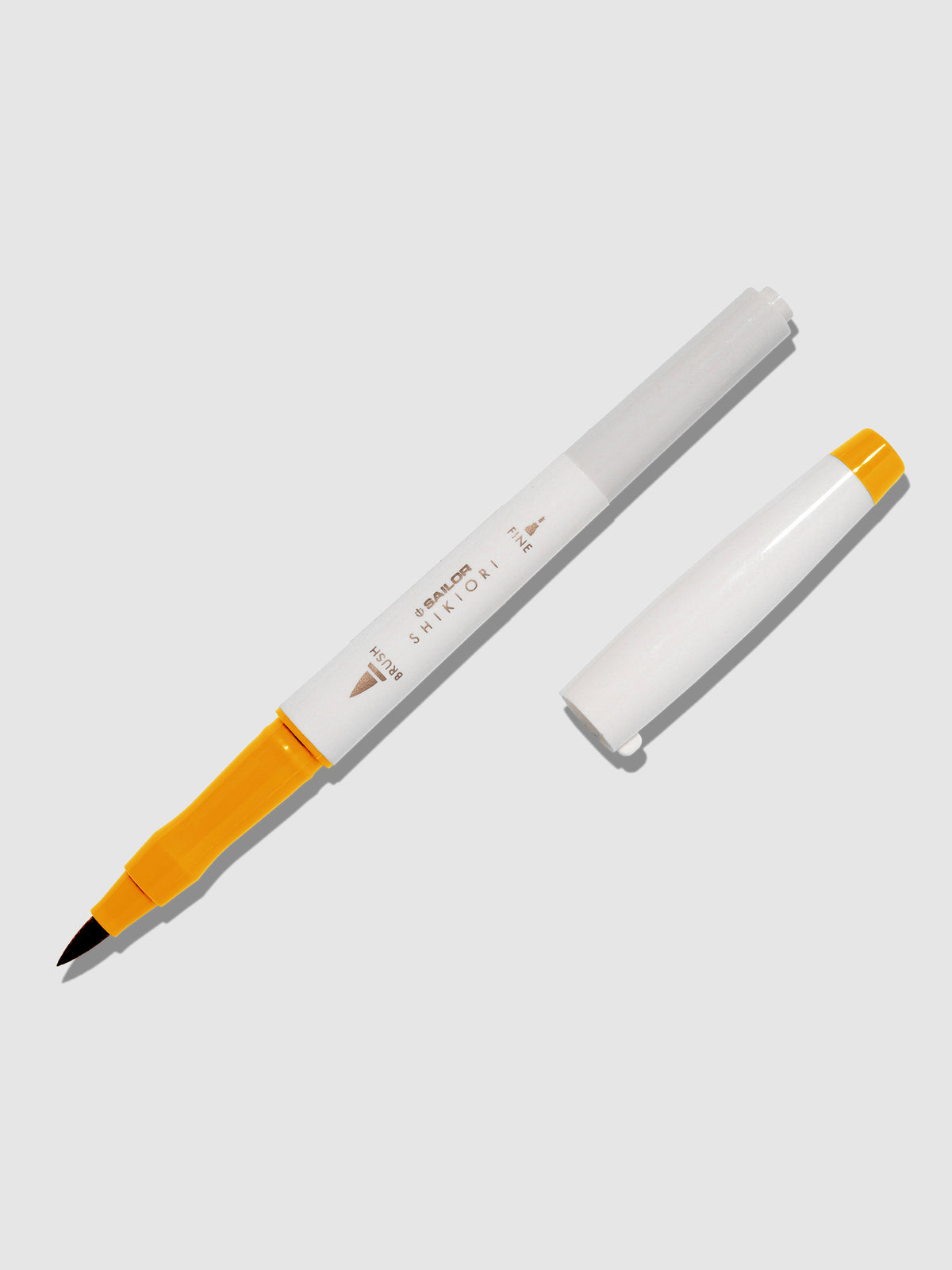 Brush pen displayed on a neutral background. It is uncapped with its brush nib exposed, and the cap lying parallel to the marker. Color pictured is Kinmokusei.