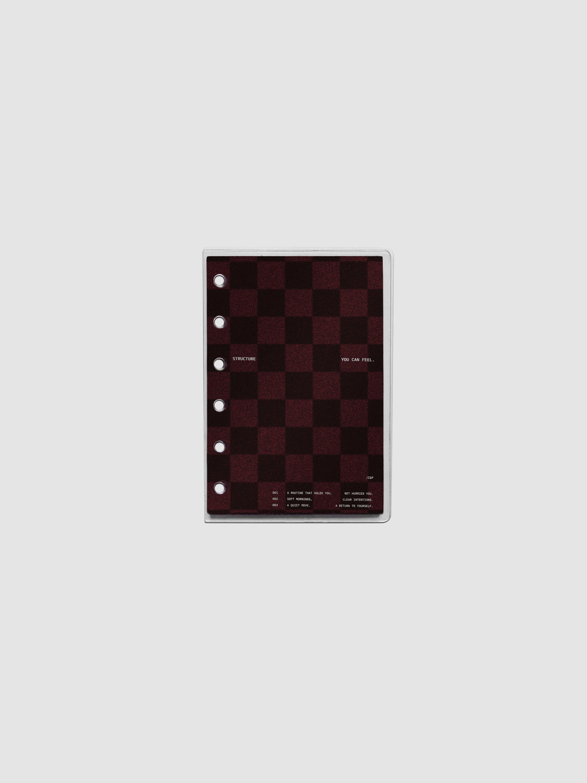 Pocket sized velvet checkered dashboard in the color Bordeaux in between two crystal clear plastic planner covers with text printed on the cover on the theme of structure and routines.