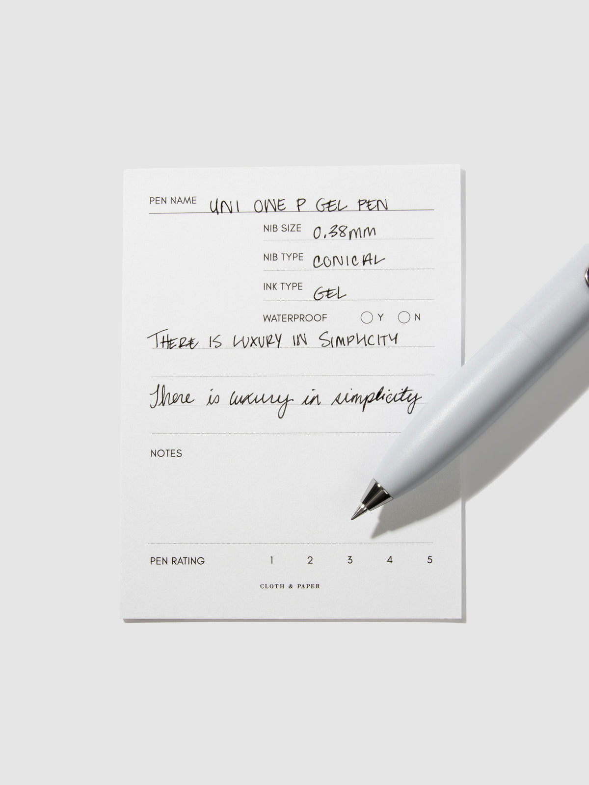 Uni-Ball One P pen resting on a pen test sheet. The sheet shows the pens specs. Color pictured is Soda.
