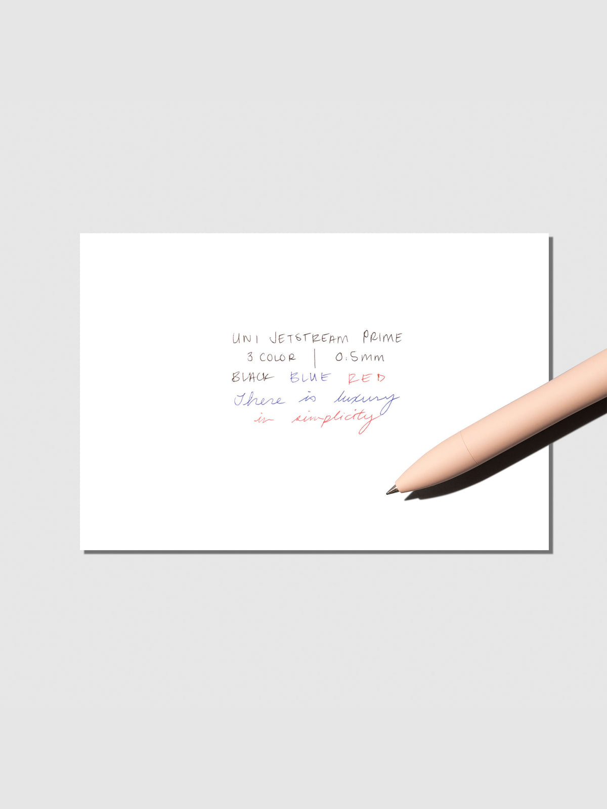 Writing sample with pen shown on a neutral background. Ink colors are black, red, and blue. Pen body color is Cotton Pink.