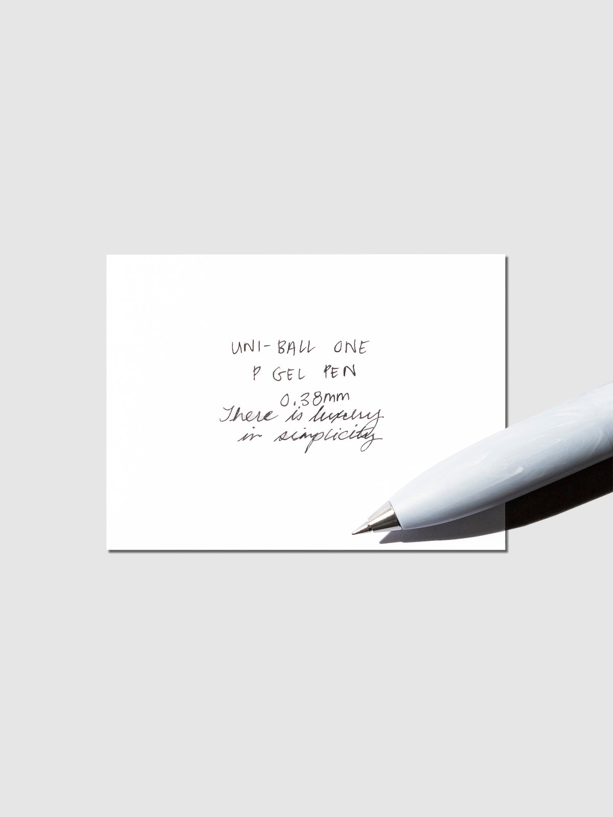 Uni-Ball One P pen resting on a pen test sheet. The sheet shows the pens specs. Color pictured is Savon.