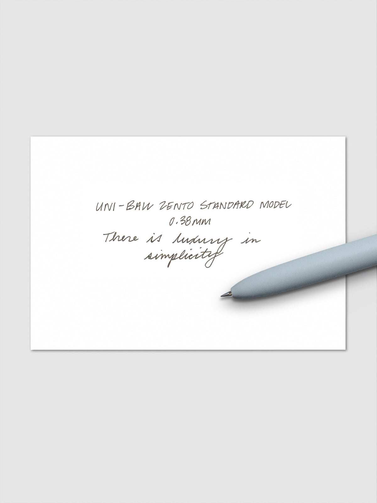Handwritten sample using the Uni-ball Zento Standard Model Pen with black ink and a 0.38 mm nib. Shown with light blue pen resting across paper.