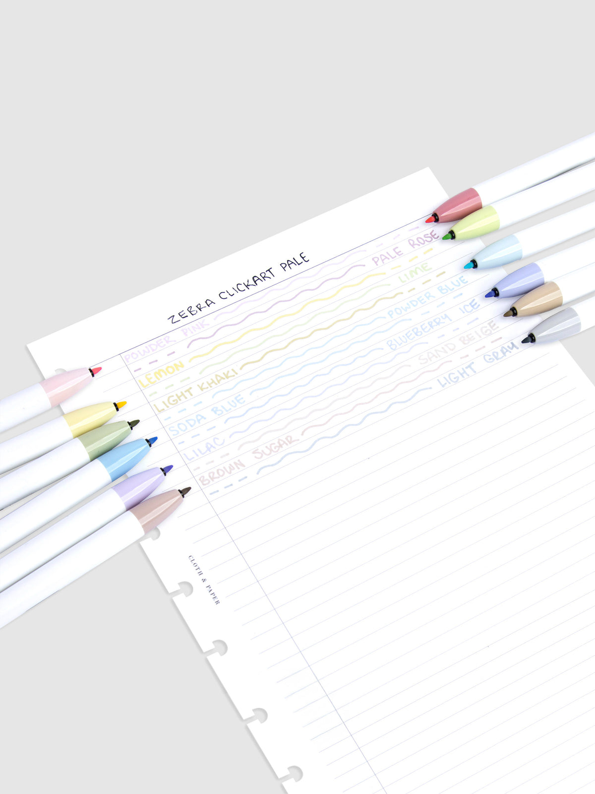 Pen test sheet showing writing and ink color examples of each marker. The 12 markers rest on the left and right edges of the sheet. The colors are Powder Pink, Pale Rose, Lemon, Lime, Light Khaki, Powder Blue, Soda Blue, Blueberry Ice, Lilac, Sand Beige, Brown Sugar, and Light Gray.