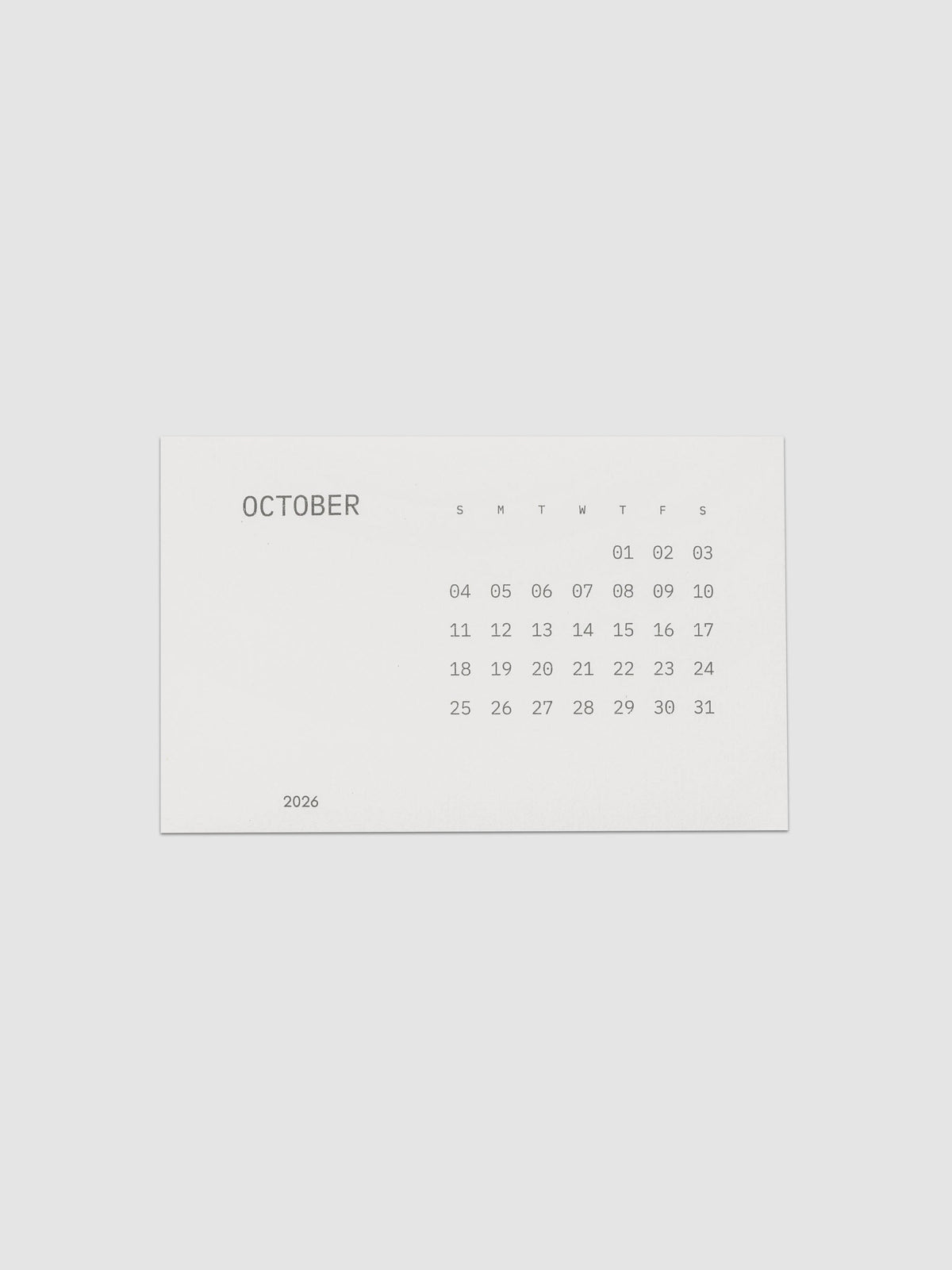 Pocket Calendar | October 2026, a small off white card printed in soft gray with the month name at the left, a full grid of dates under single letter weekday headers, and the year set at the lower left