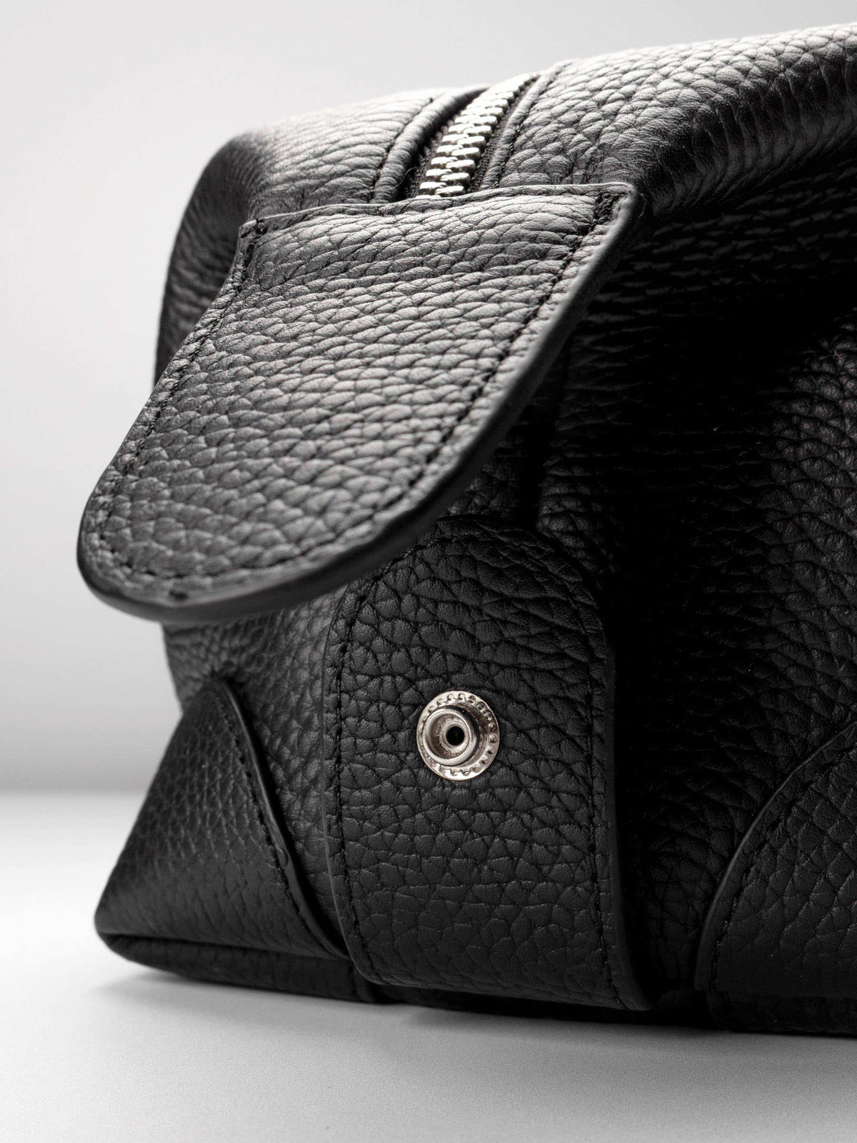 Folded Form Pouch close-up of silver snap hardware on side panel with leather zipper pull and silver zipper visible above