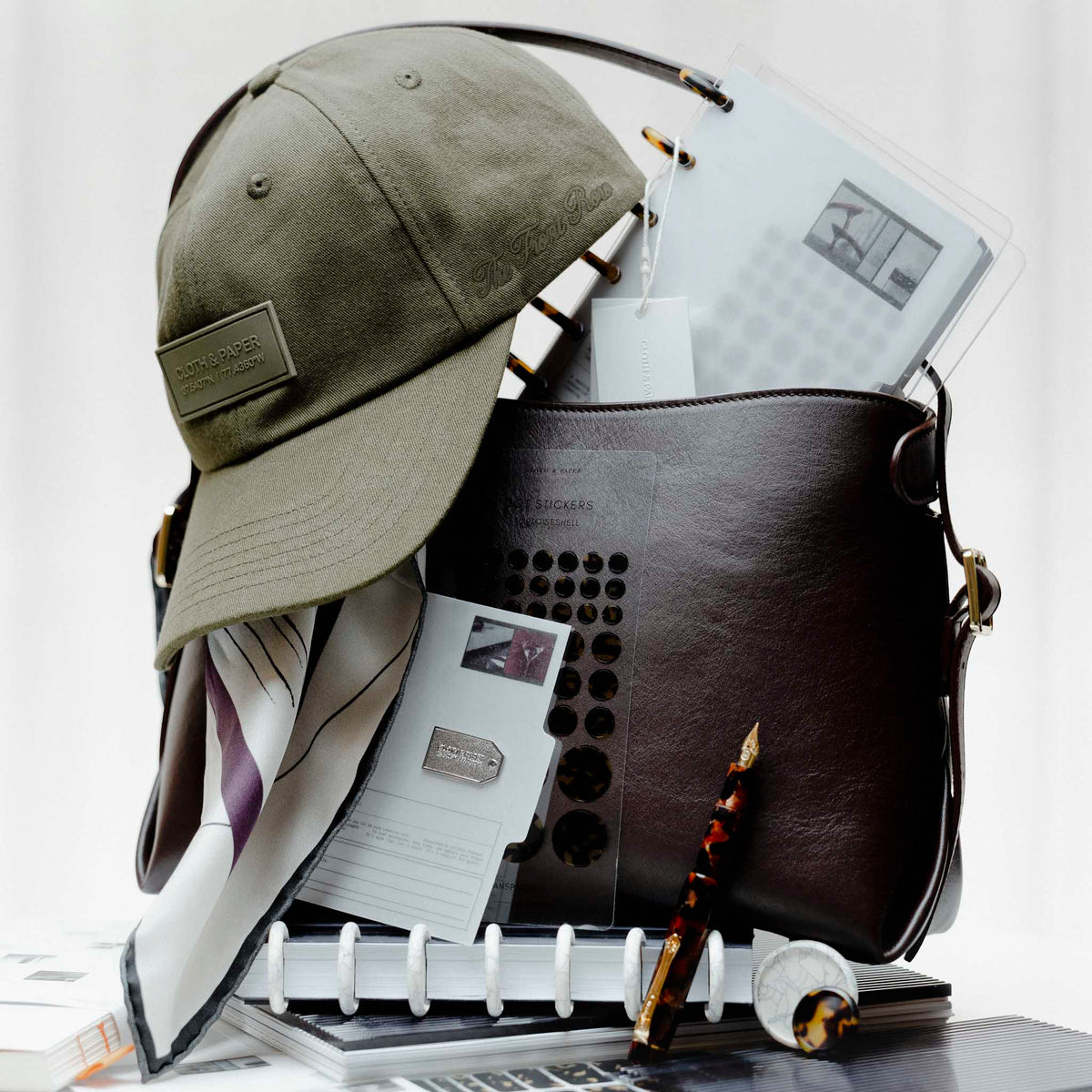 Several Planner Essentials and accessories from the Front Row Collections staged inside a Valencia Bag.  Heavily featured are the Label Hat, Planner Brooch | Tag, and Kaweco Art Sport Fountain Pen in Hickory Brown.