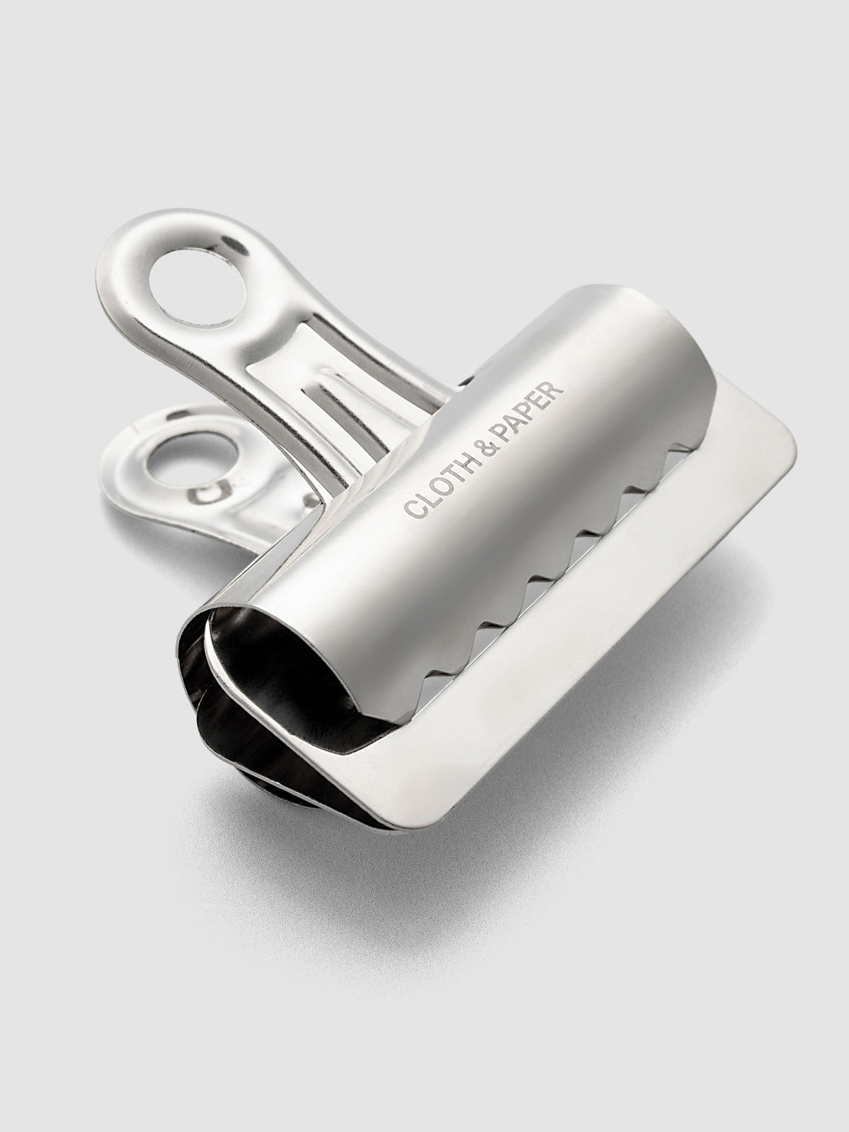 Silver metal notebook clip with Cloth & Paper logo etched onto the surface.