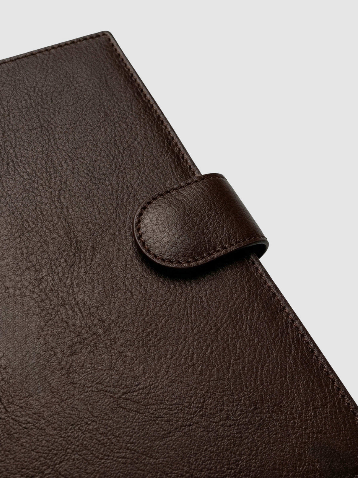 Detail of gold magnetic snap closure securing a dark brown genuine leather A5 planner cover shut