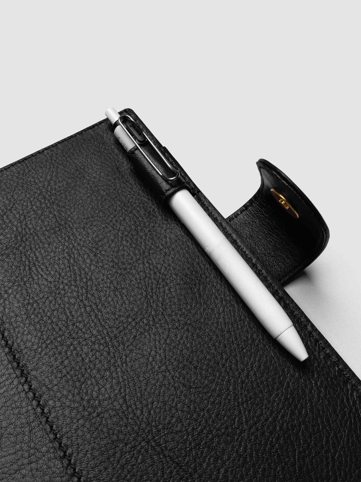 Detail of a pen threaded through the pen loop on the right interior of a black genuine leather Personal Wide 6-ring planner cover