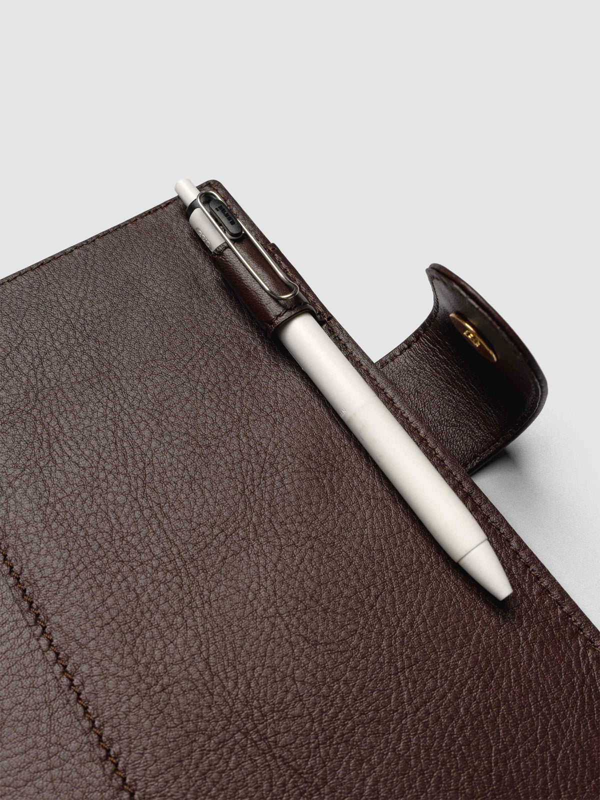 Detail of a pen threaded through the pen loop on the right interior of a dark brown genuine leather Personal Wide 6-ring planner cover