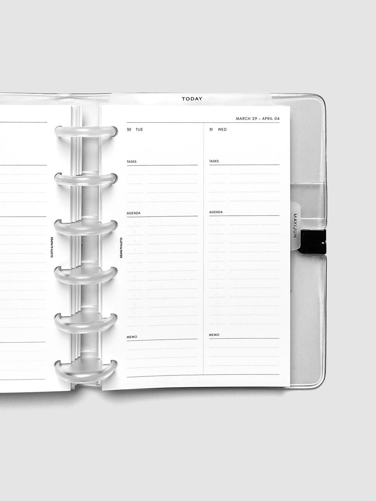 Close-up of an open planner with clear 6-disc binding, weekly spread showing Tuesday and Wednesday daily columns with tasks, agenda, and memo sections, tabbed monthly dividers visible at the edge, CP Petite 6-Disc Punch size