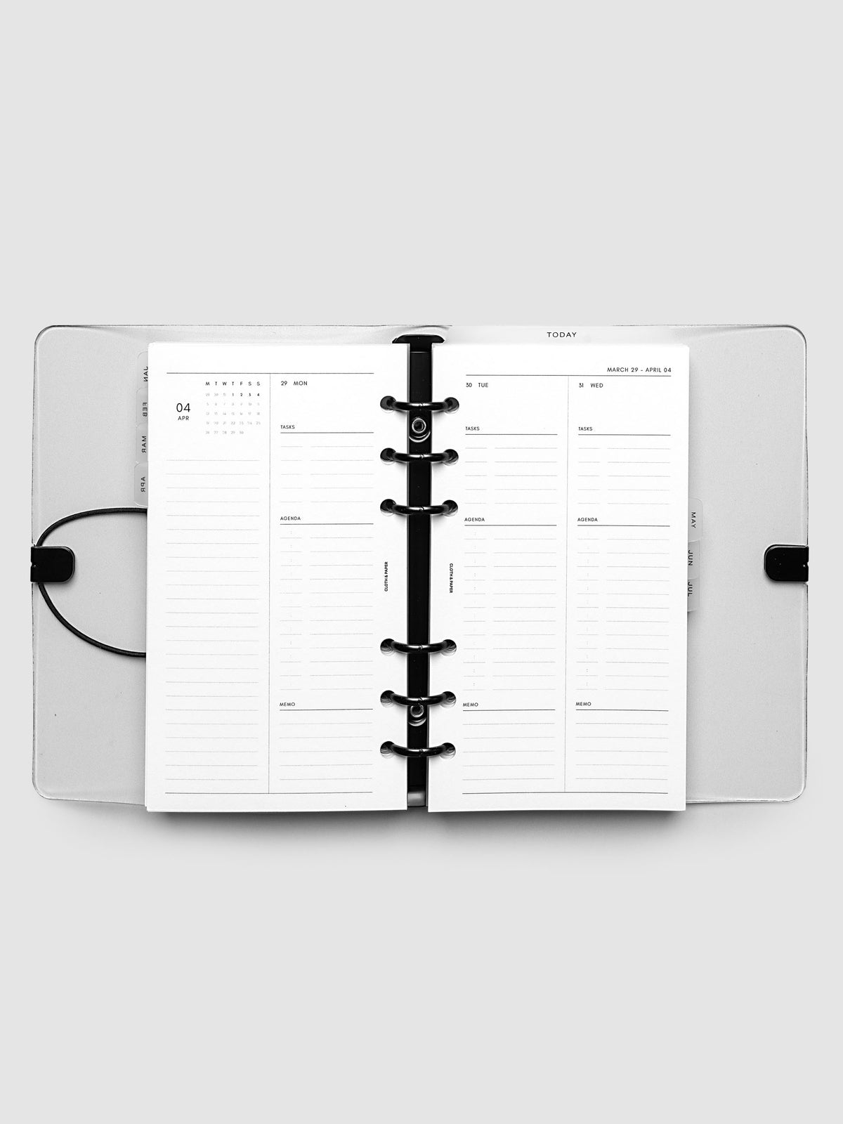 Flat lay of an open planner with black 6-ring binding at the center, a Monday through Wednesday spread across two facing pages with a mini monthly calendar, daily tasks, agenda, and memo sections, Personal 6-Ring Punch size