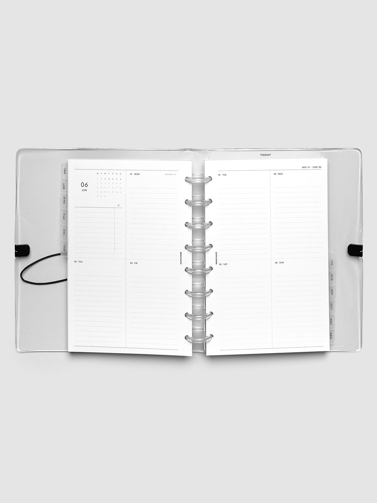 Flat lay of an open planner with clear 8-disc binding at the center, a Monday through Sunday weekly vertical spread across two facing pages with a mini calendar and lined daily sections, Half Letter 8-Disc Punch size