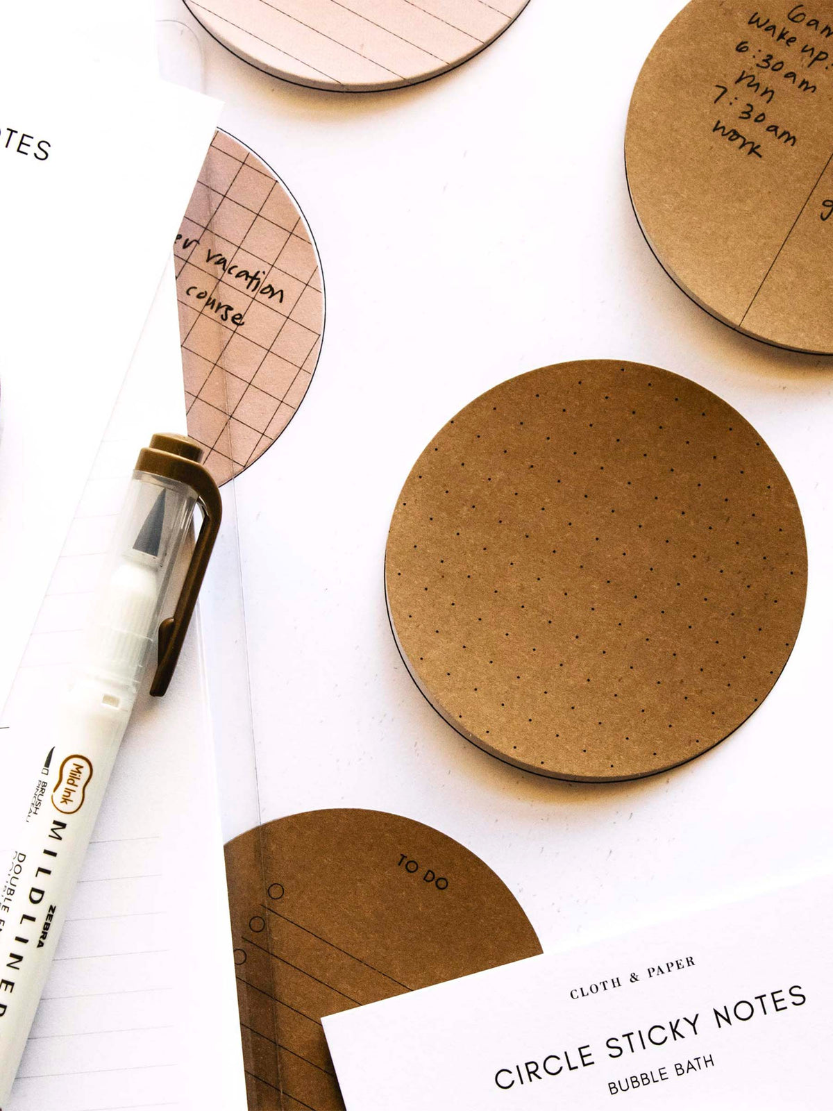 Sticky notes printed using Circle Sticky Note Printable in Essentials layered on a table with a planner, Zebra Mildliner Brush Pen, and blank sticky note pads. Sticky notes are brown and pink.