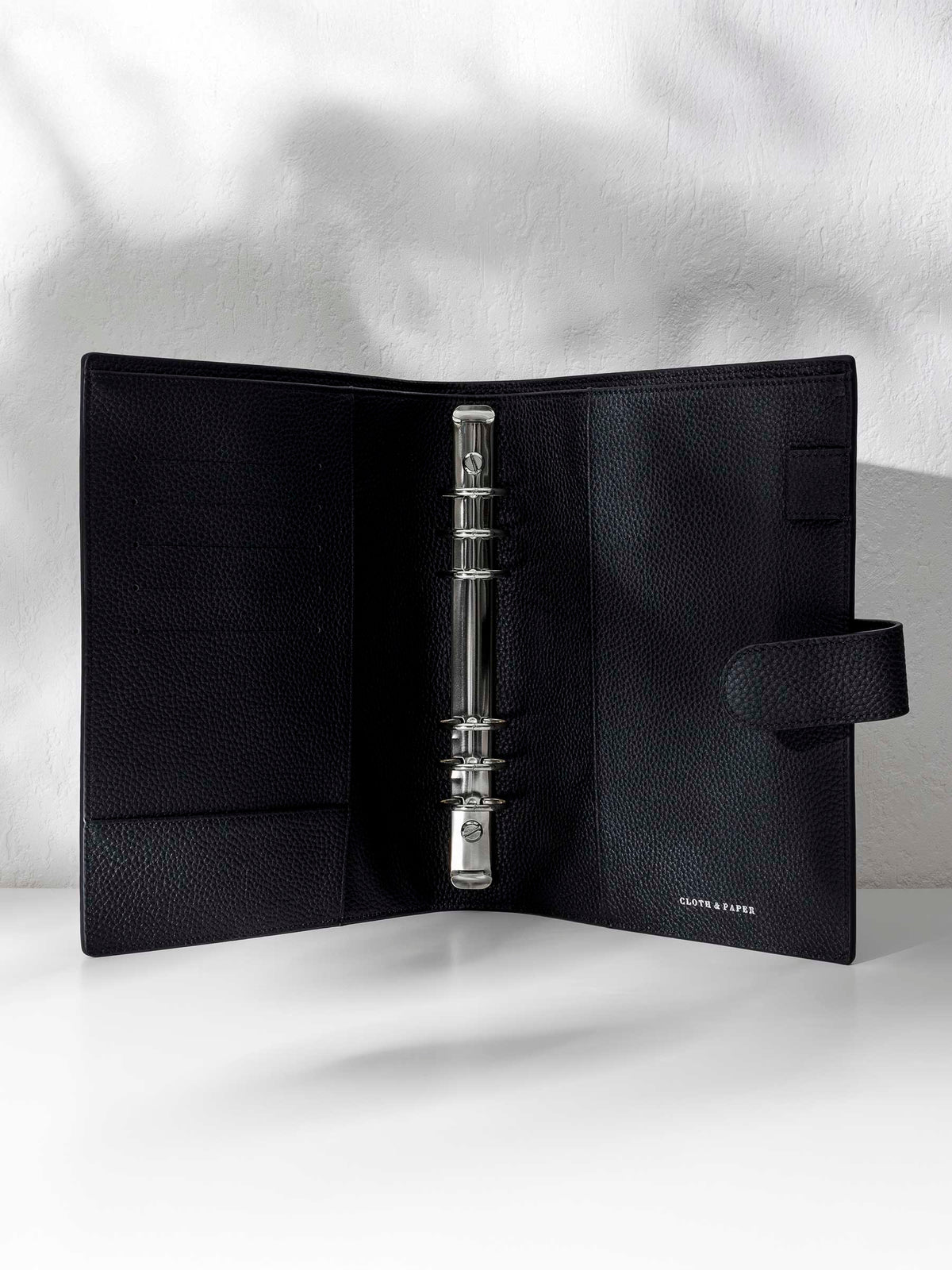 Black leather agenda displayed against a shadowed background. It is opened to show off the silver hardware and company logo stamp.