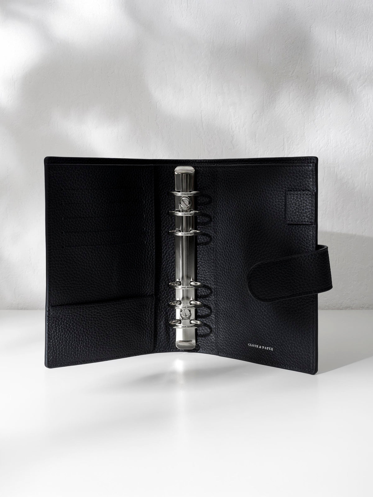 Black leather agenda displayed against a shadowed background. It is opened to show off the silver hardware and company logo stamp.
