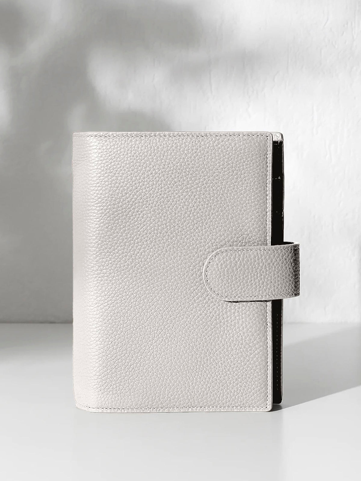 A closed ash leather planner with a closure displayed against a shadowed background.