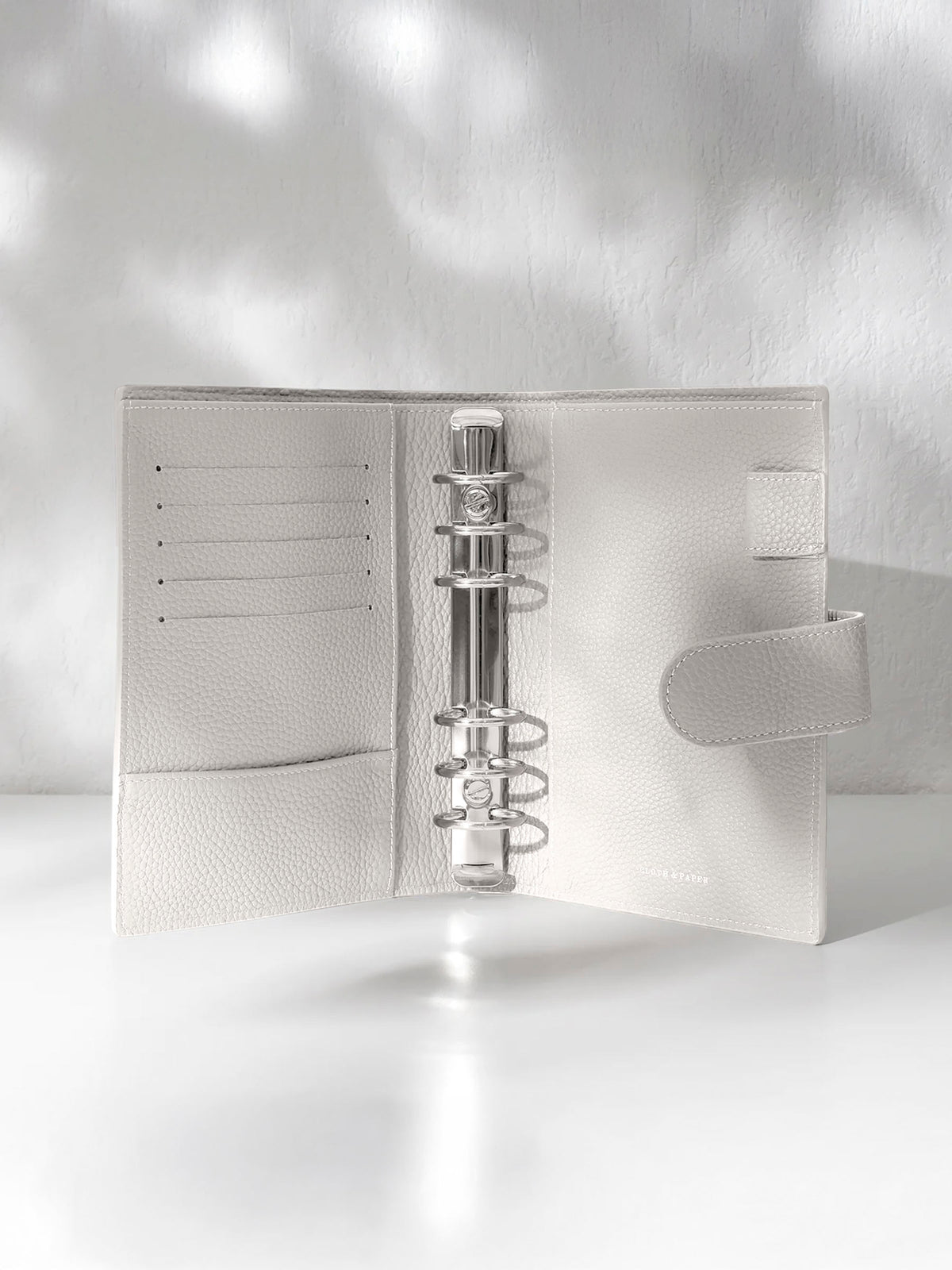 Ash leather agenda displayed against a shadowed background. It is opened to display the silver hardware and company foil stamp.