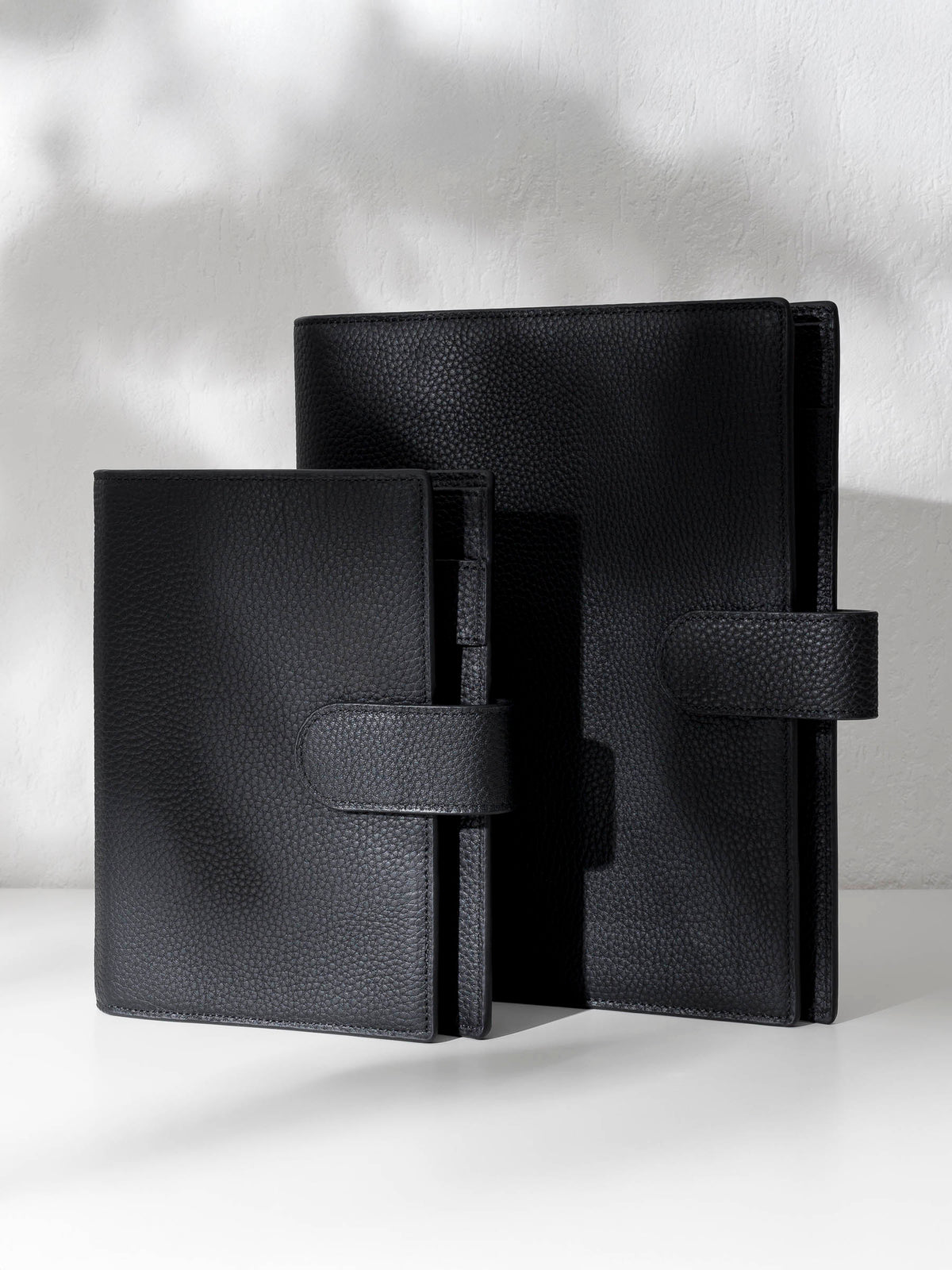 Two black leather agendas displayed against a shadowed background.
