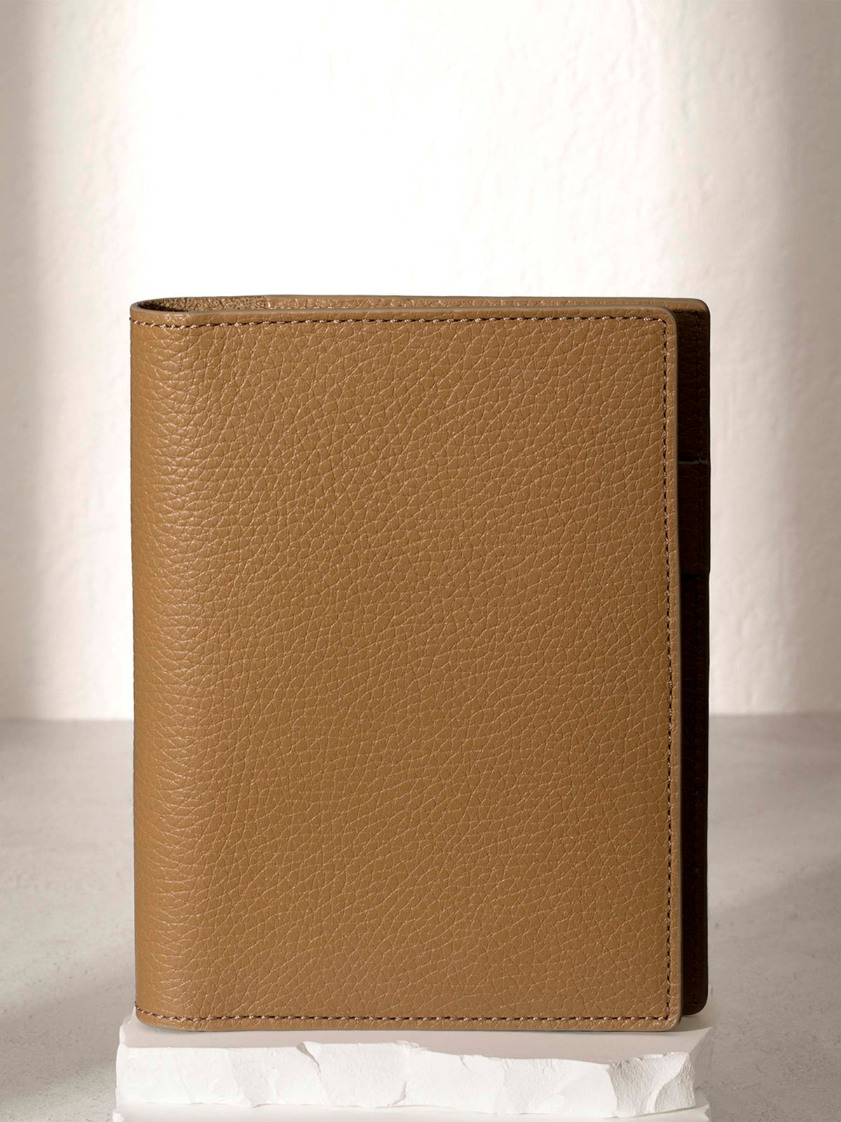 CP Petite Catalonia folio displayed on a white stone pedestal. The background is a natural textured off-white material, and a spotlight behind the folio highlights its placement.