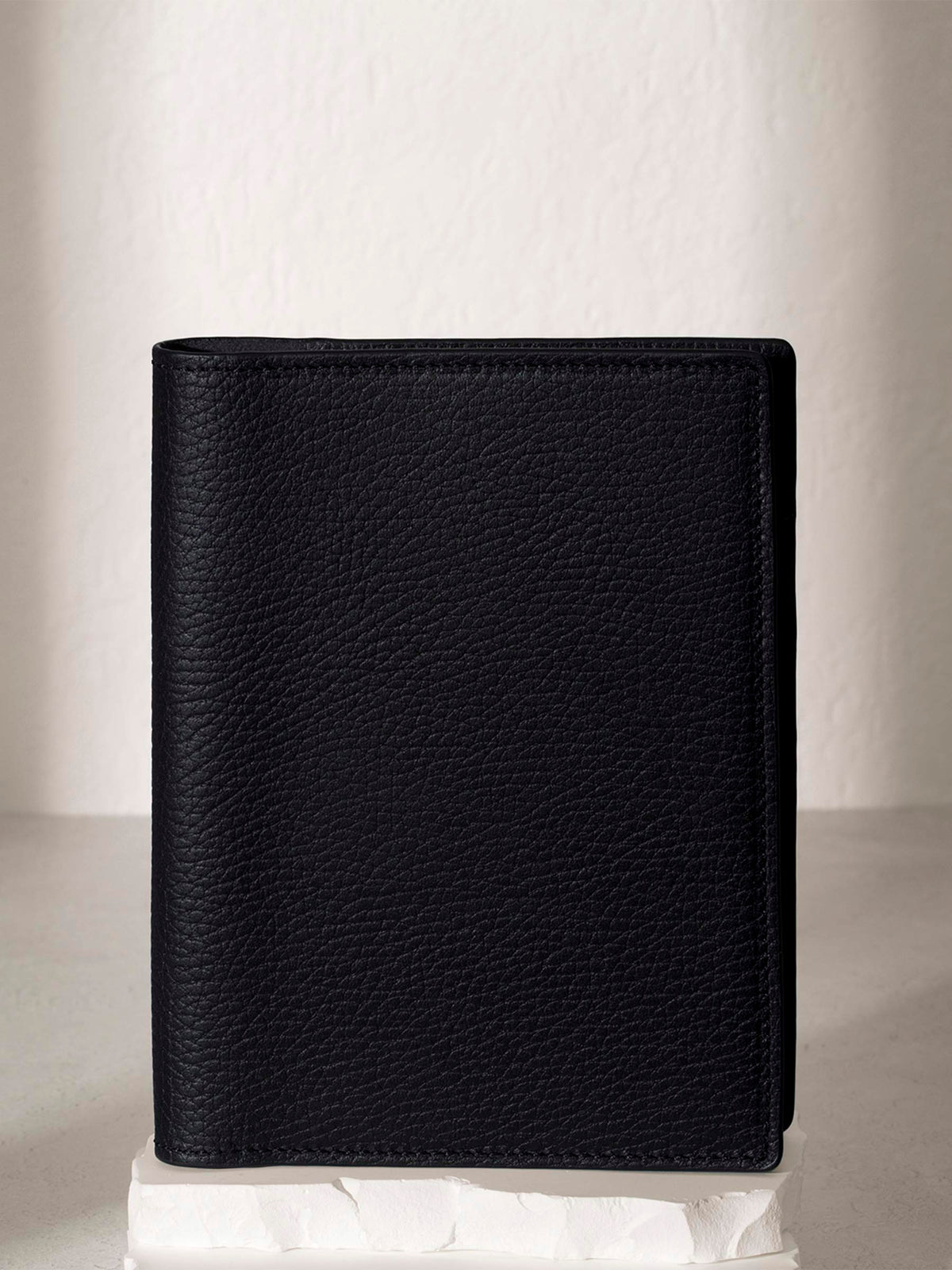Heirloom Leather Folio, CP Petite, Cloth and Paper. Padrillo folio displayed on a white stone pedestal. The background is a natural textured off-white material, and a spotlight behind the folio highlights its placement.