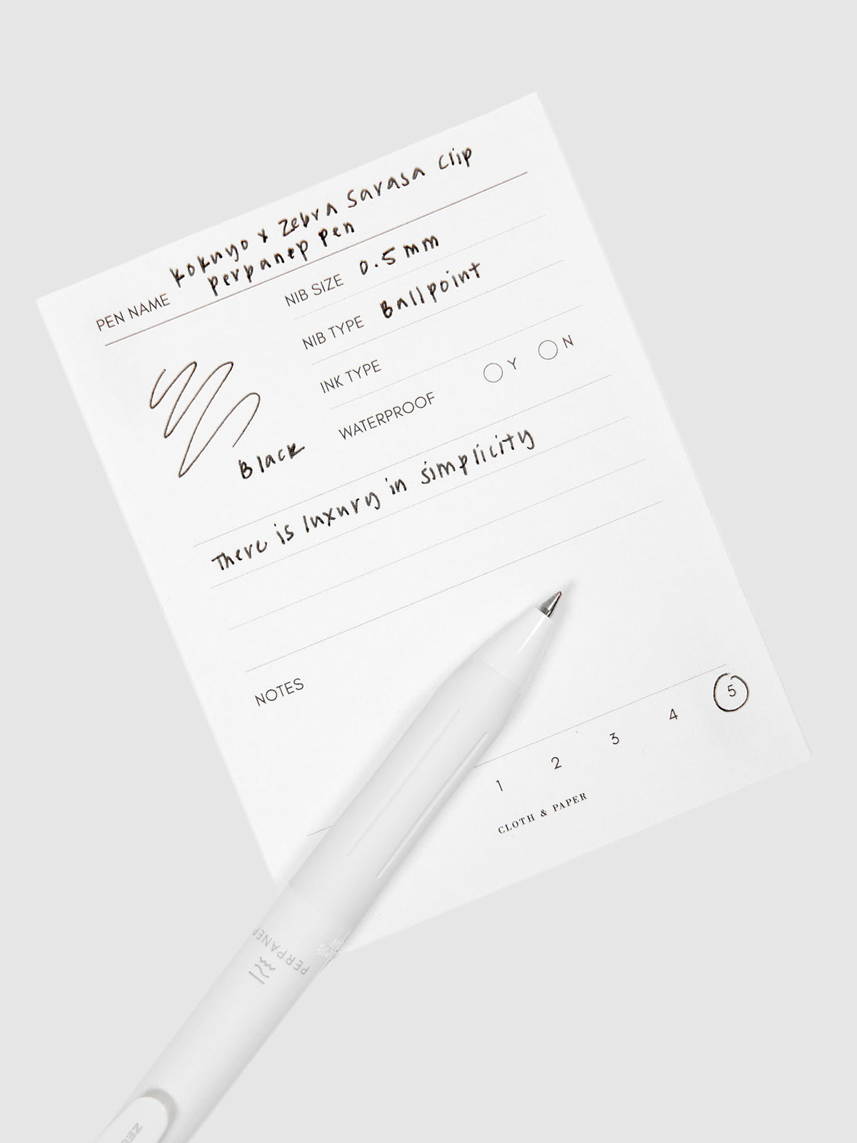 Kokuyo x Zebra Sarasa Clip Perpanep Pen, Cloth and Paper. Pen resting on pen test sheet displaying writing sample.
