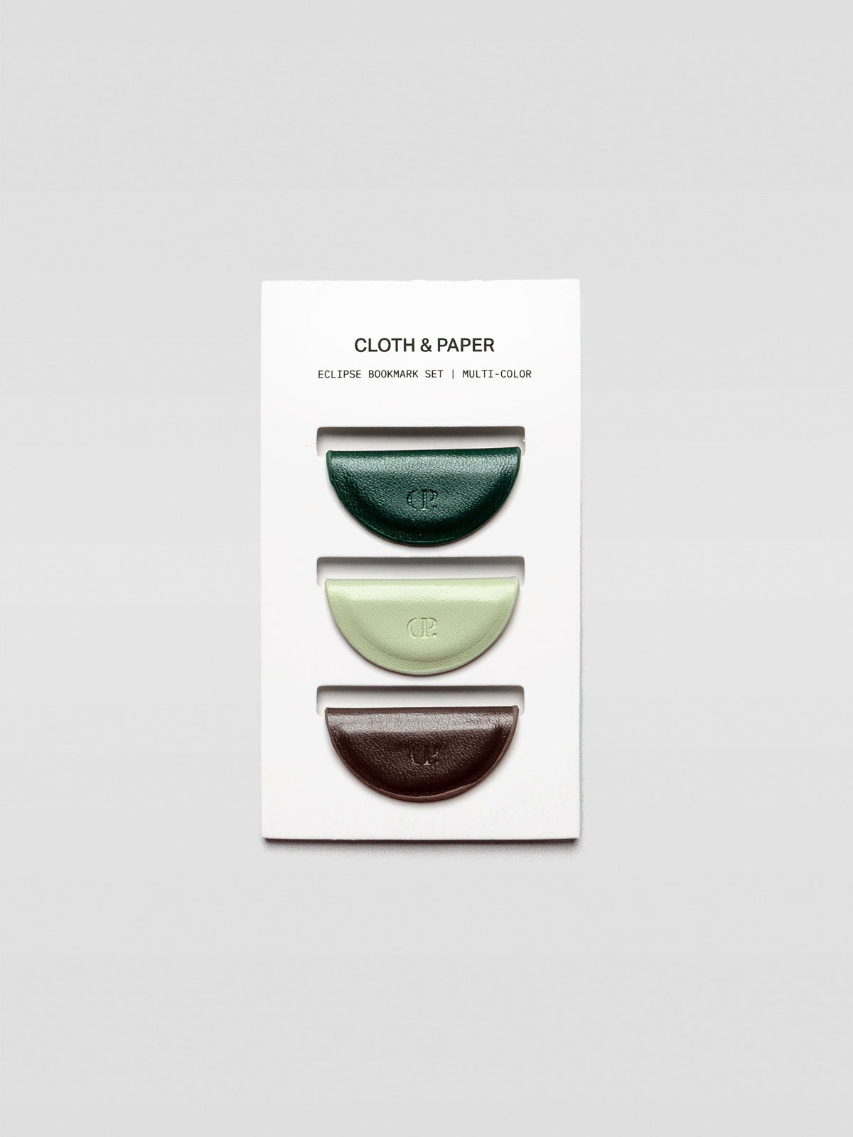 Three half-moon magnetic bookmarks in dark green, pale mint, and deep brown arranged vertically on a white Cloth & Paper branded backing card.