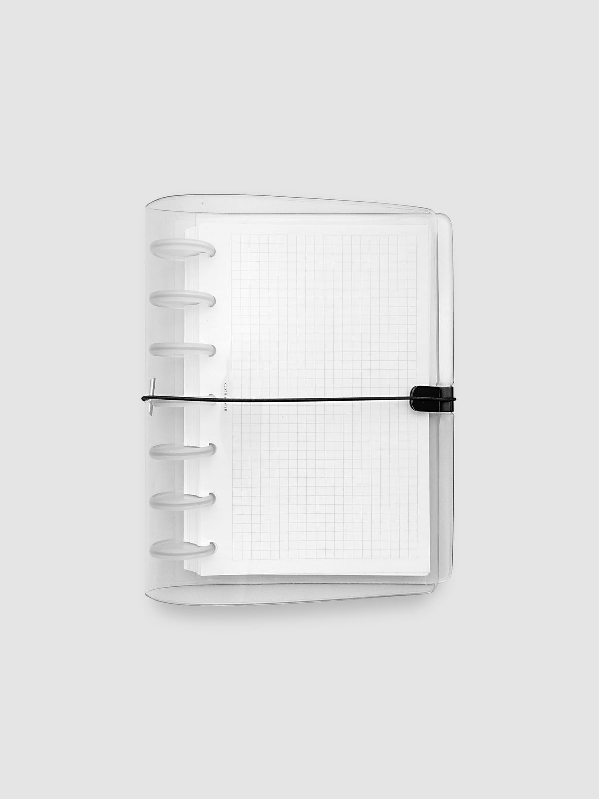 A clear plastic notebook cover with a black elastic closure band, with a discbound planner and grid inserts inside, against a light gray background.