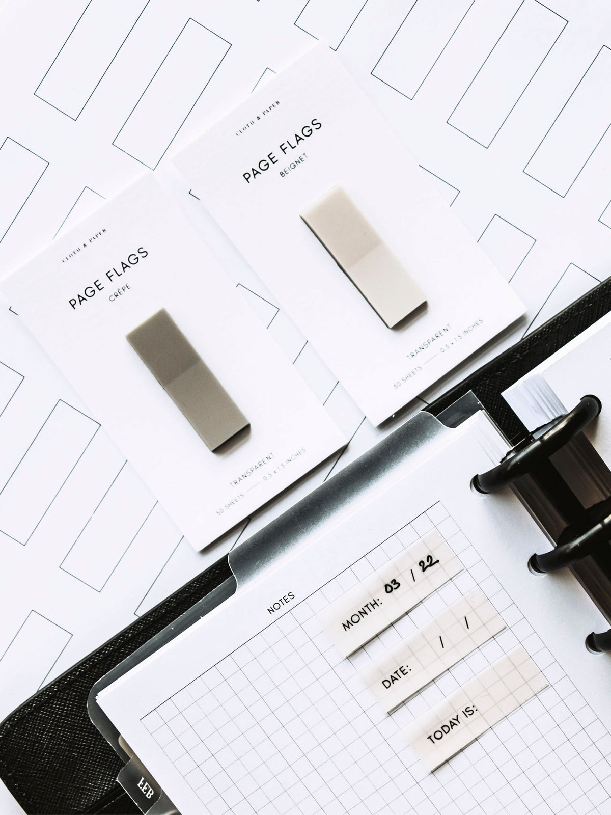 Printed page flags in use inside a discbound planner. Two pads of page flags are resting on a table next to the planner.