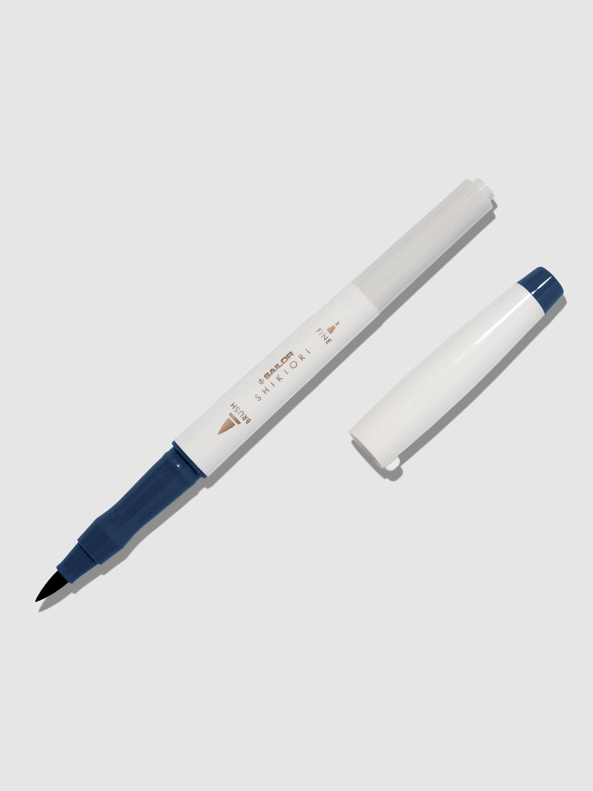 Brush pen displayed on a neutral background. It is uncapped with its brush nib exposed, and the cap lying parallel to the marker. Color pictured is Yonaga. 