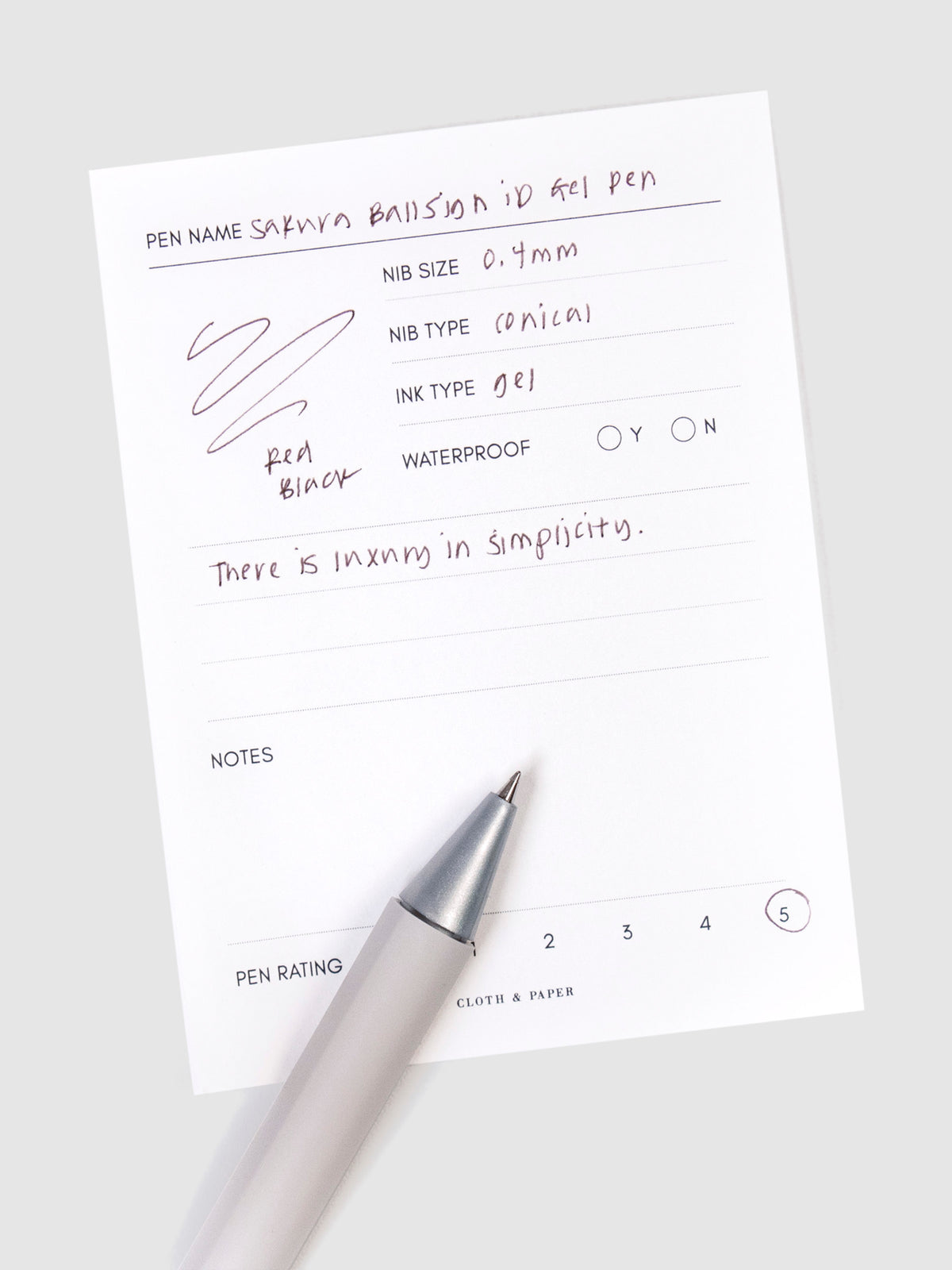Sakura Ballsign iD Gel Pen, 0.4 mm, Cloth and Paper. Red black pen resting on pen test sheet displaying writing sample.