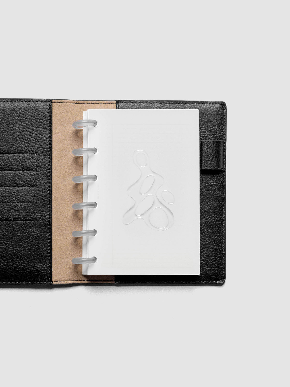 Light grey, semi-transparent, and glossy plastic planner dashboard with organic raised shape design in size CP Petite shown discbound in a black leather folio.