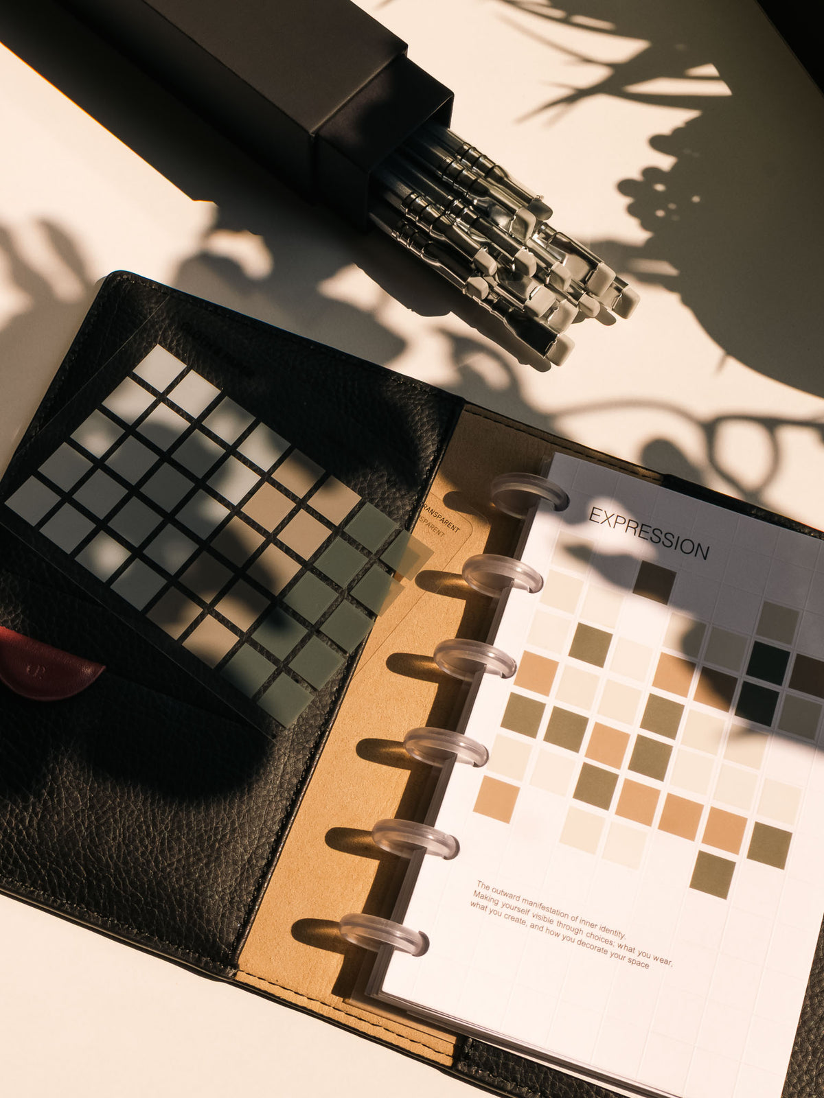 Overhead flatlay of a workspace featuring the Tile Planner Dashboard partially decorated with Square Stickers, alongside a box of pencils. 