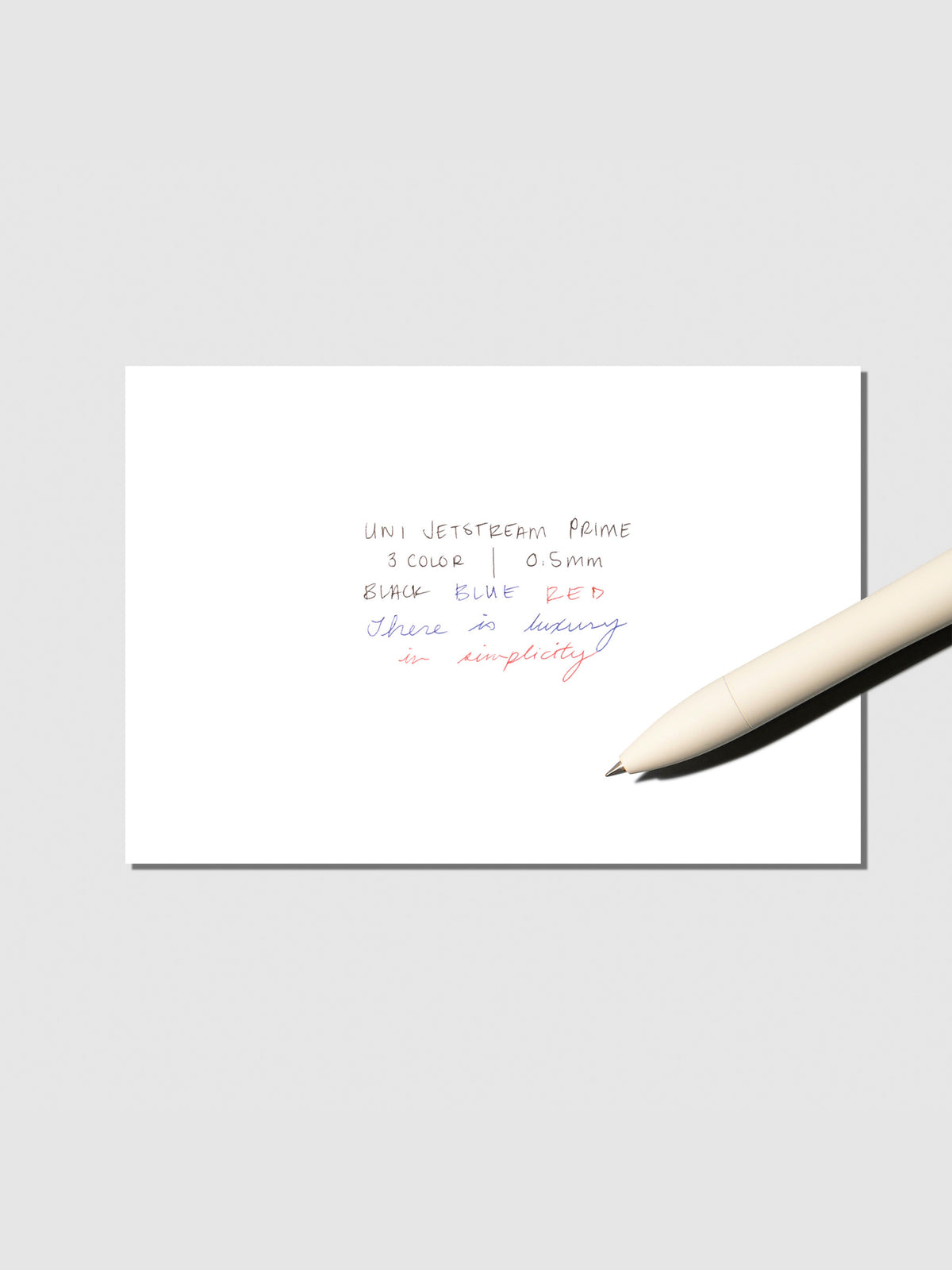 Writing sample with pen shown on a neutral background. Ink colors are black, red, and blue. Pen body color is Cloudy White.